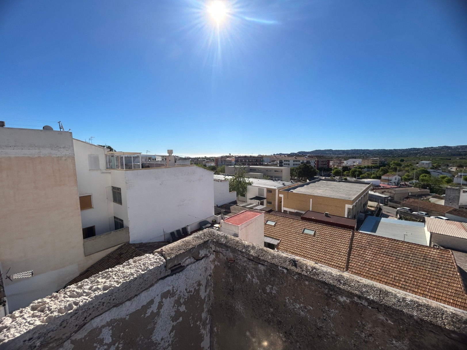 Panoramic views from the rooftop overlooking the Jávea town center and the Mediterranean Sea, featuring traditional tiled roofs and distant mountain silhouettes.