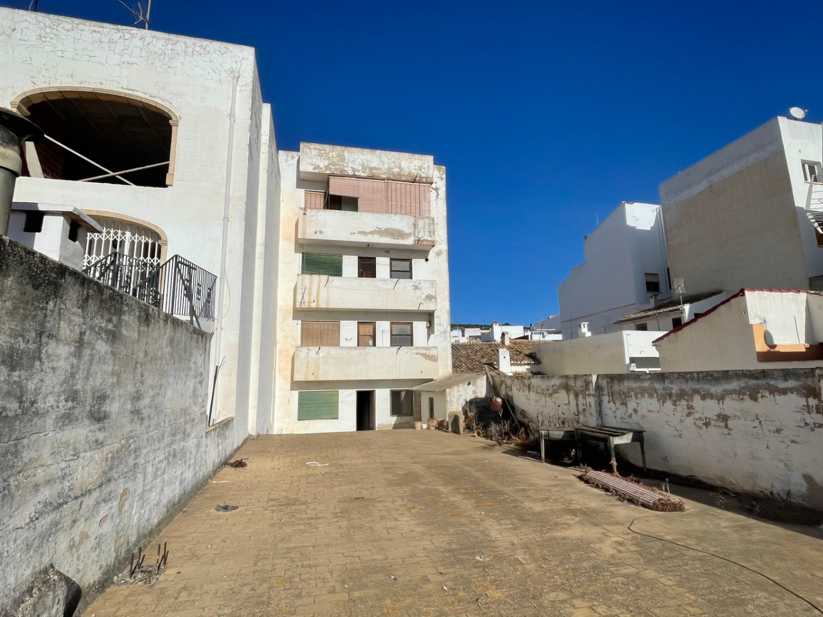 Rear view of the four-story building featuring a large paved courtyard and perimeter walls. The facade displays original balconies and windows under bright natural light.