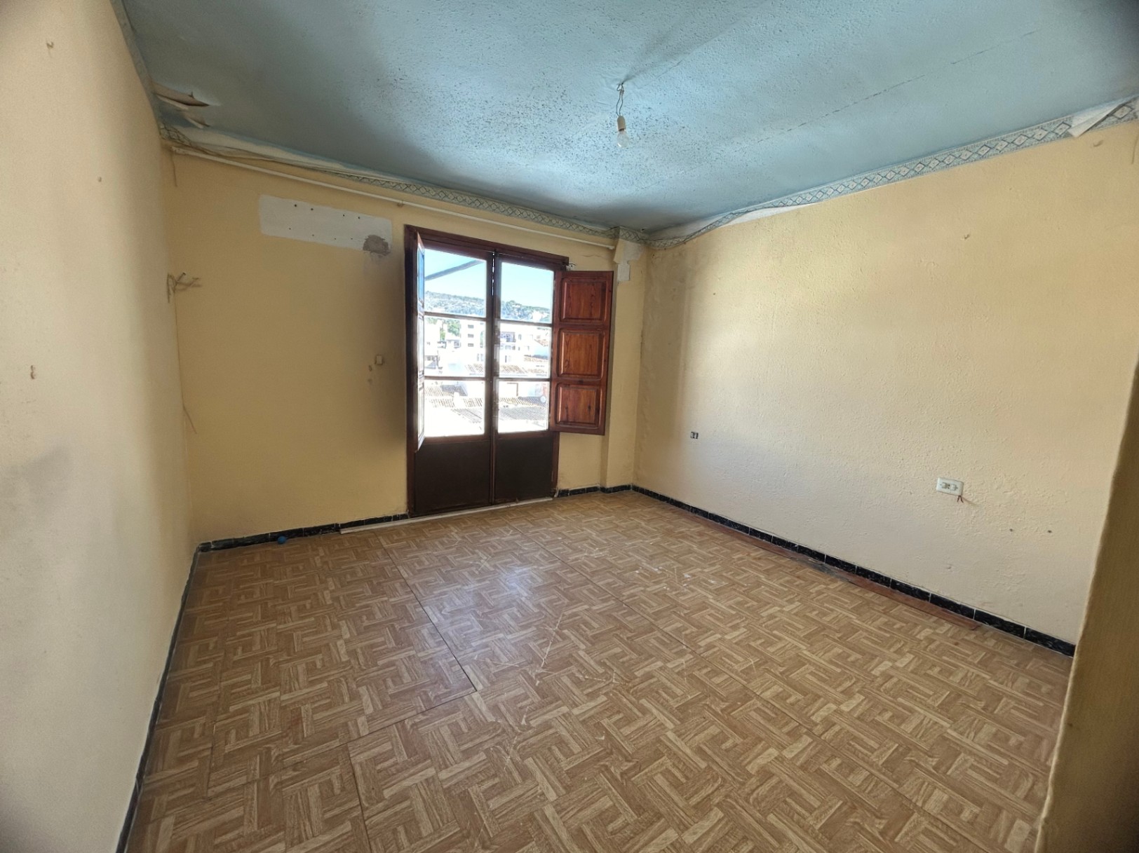 Room for renovation featuring patterned ceramic tile flooring, cream walls, and wooden double doors opening onto a balcony with urban views.