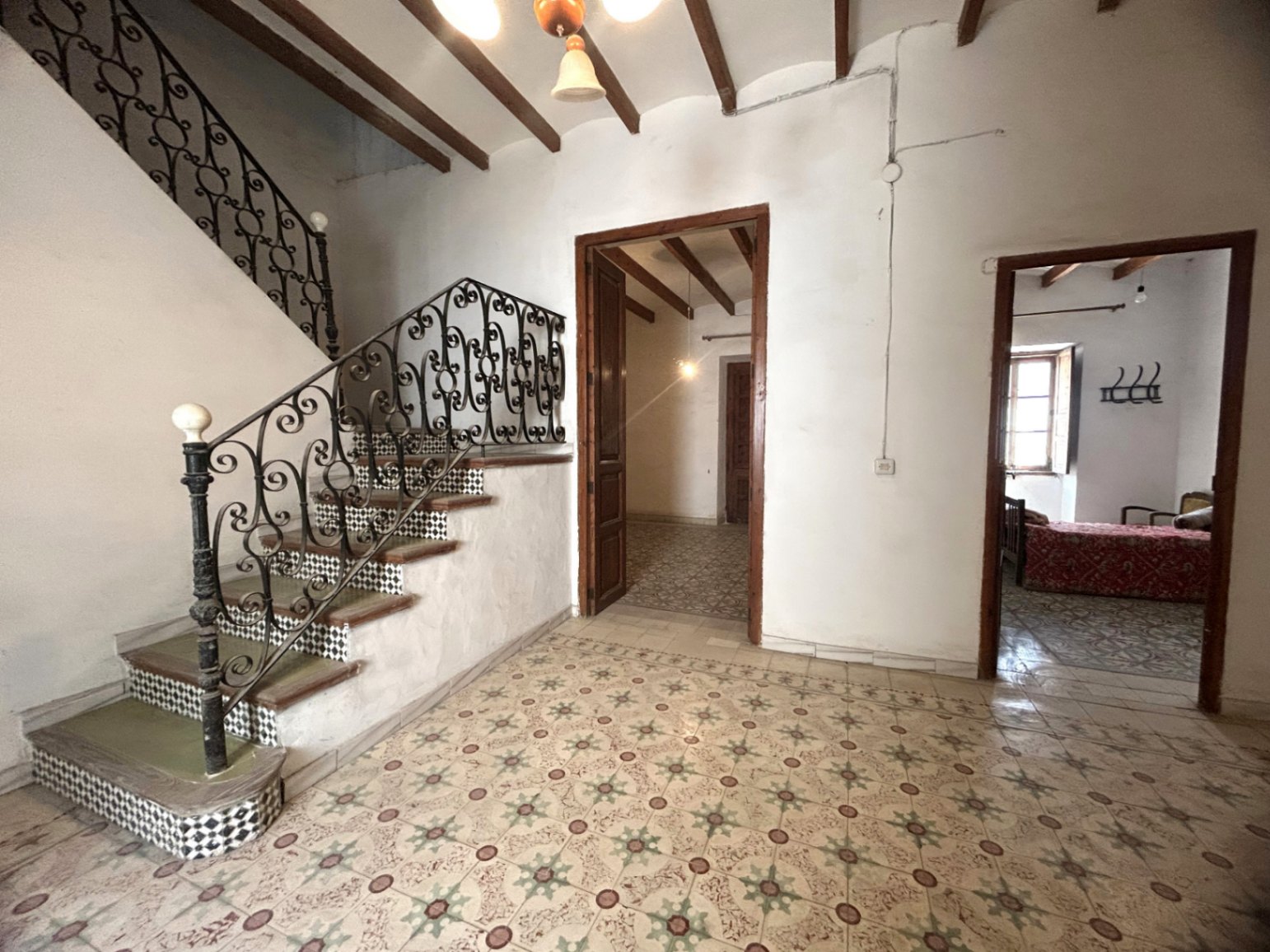 Main entrance hall featuring original hydraulic tile flooring, exposed wooden beams, and a grand staircase with ornate wrought iron railings and tiled risers.