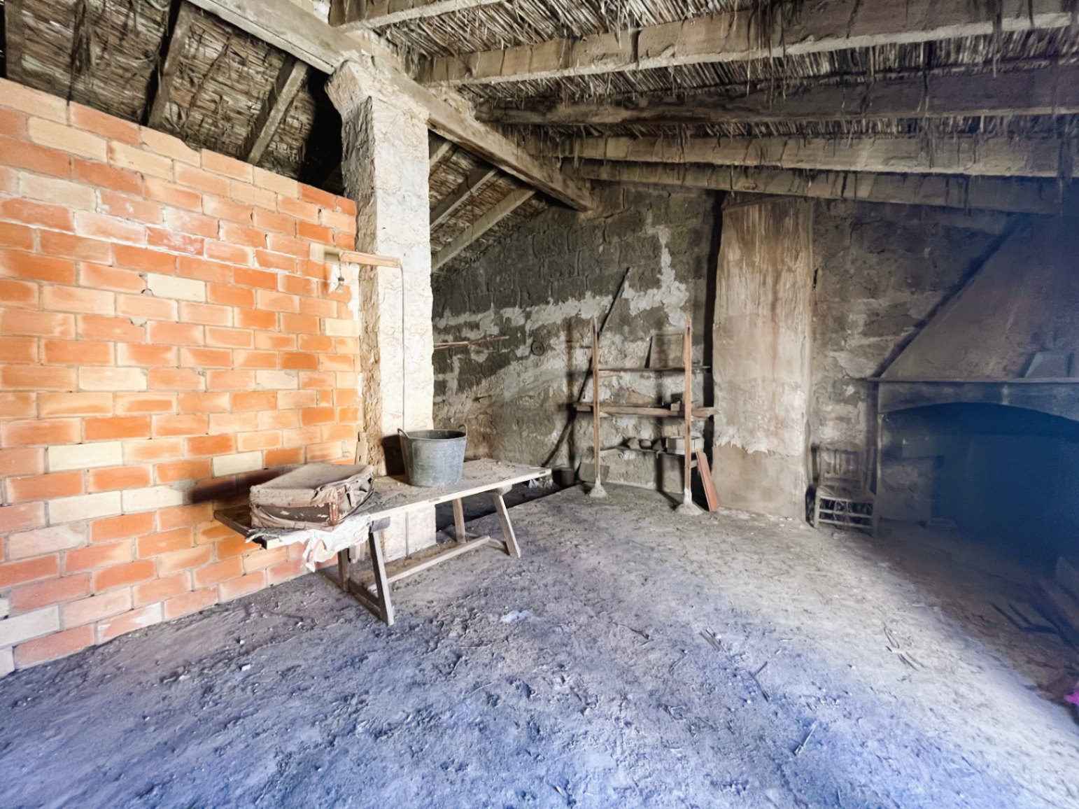 Open-plan attic featuring original reed ceilings and wooden beams. This rustic space includes a stone fireplace and offers significant renovation potential.