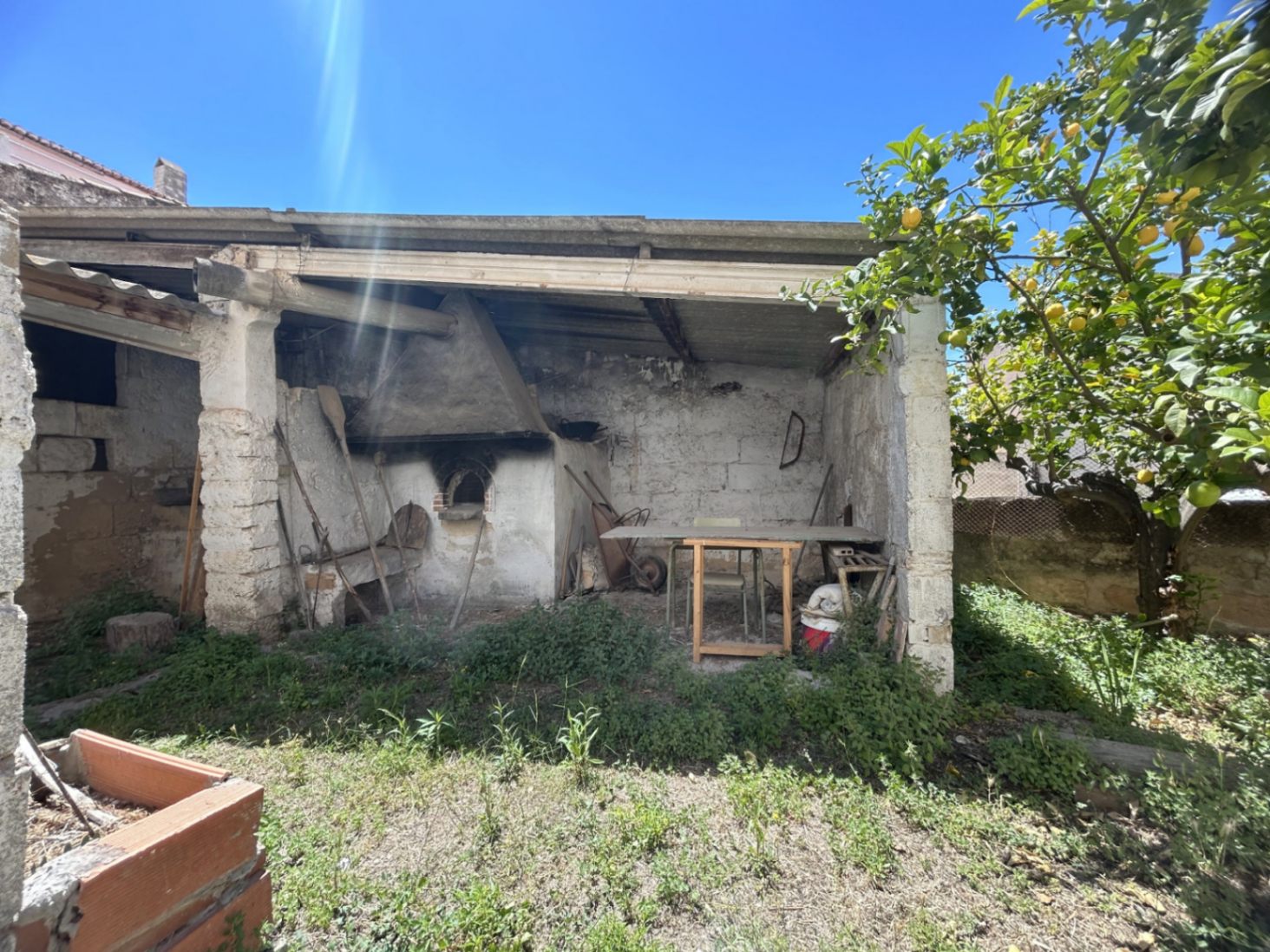 Outdoor courtyard featuring a traditional wood-fired oven and rustic stone porch, adjacent to a mature lemon tree in the property's garden area.
