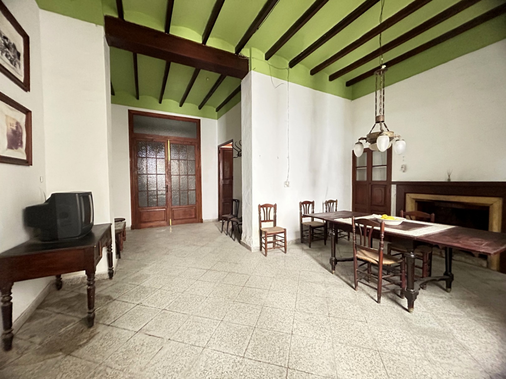 Spacious dining area featuring high ceilings with exposed dark wood beams, green accents, and terrazzo flooring. Includes a traditional fireplace and large wooden double doors.