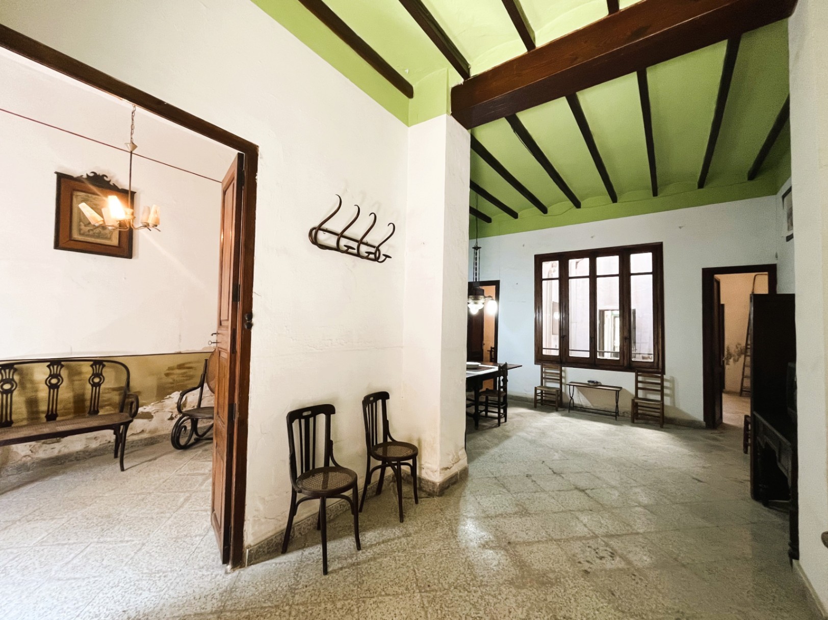 Spacious entrance hall featuring exposed wooden beams on a green ceiling, original stone flooring, and views into adjacent rooms with period furniture and interior windows.