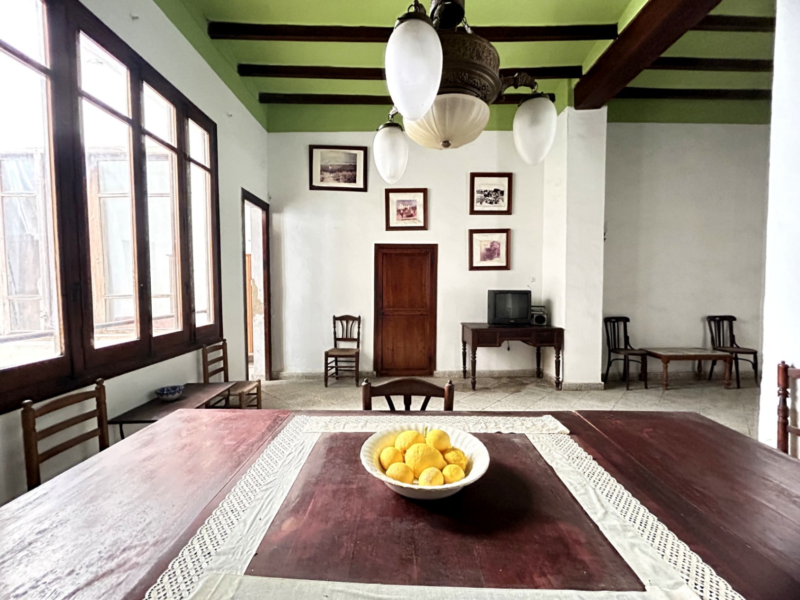Traditional dining area featuring high ceilings with exposed dark wood beams, period windows, and a vintage glass chandelier in a historic setting.