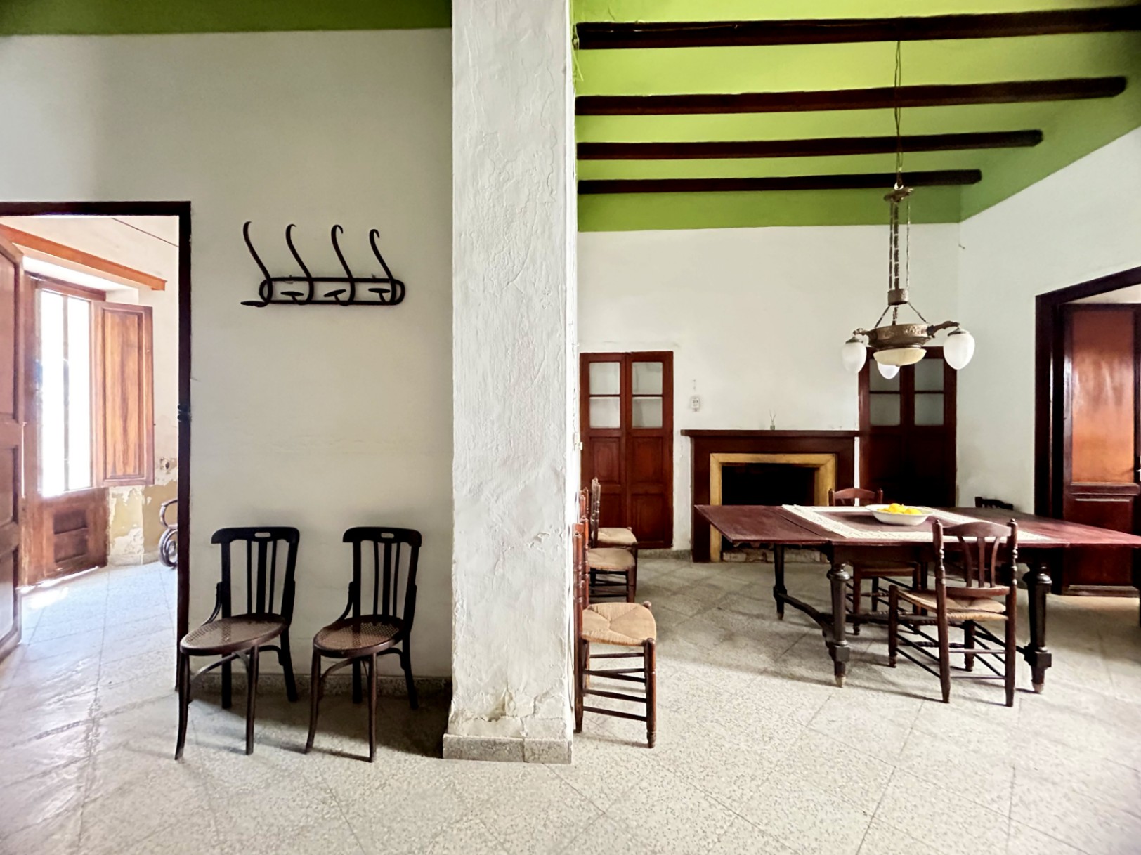 Traditional dining room featuring original wooden beams, high green ceilings, and a classic fireplace. Period furniture and natural light from adjacent rooms define the space.
