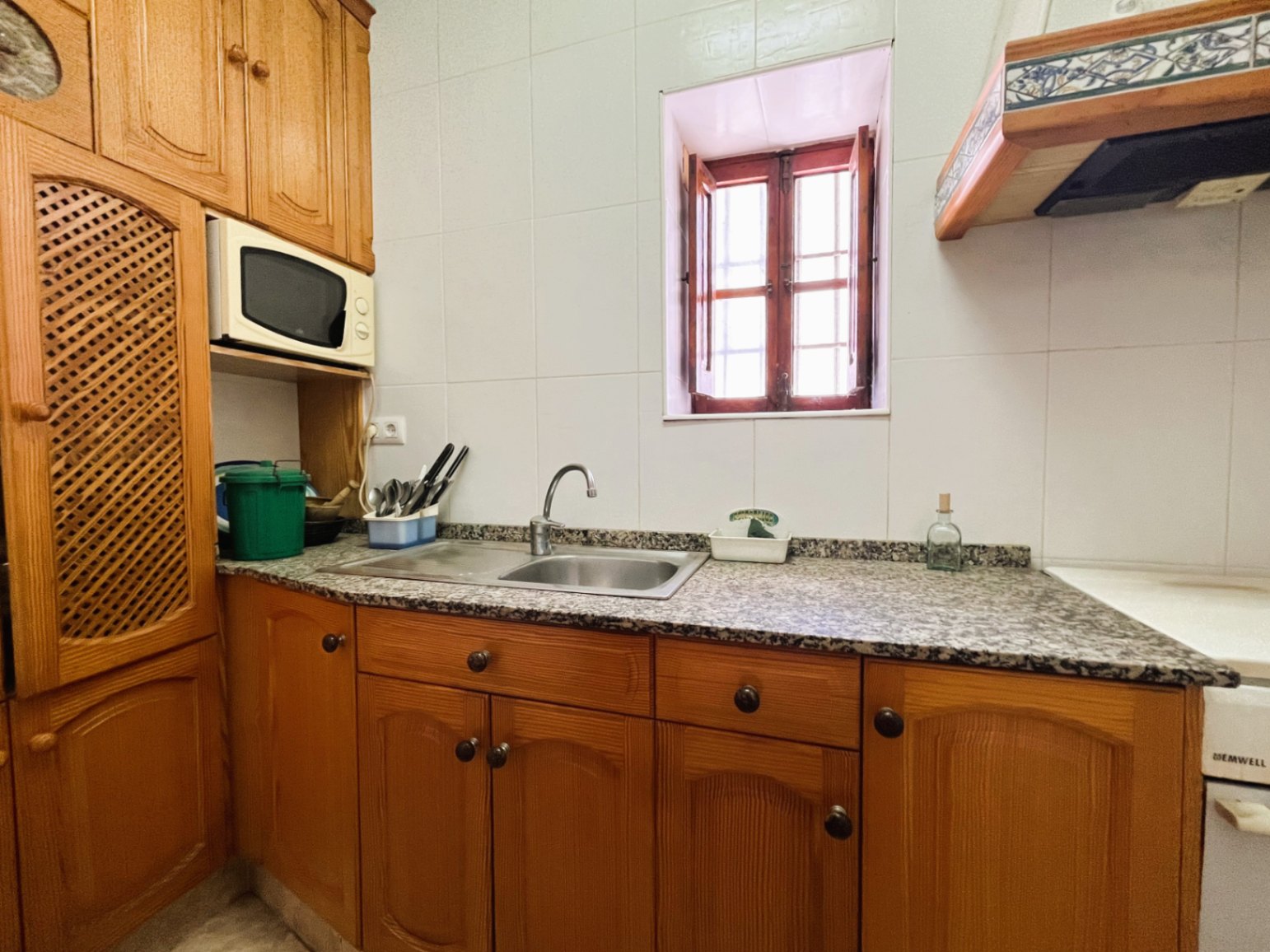 Closed kitchen featuring traditional wooden cabinetry, a granite countertop with a double sink, and a small window with classic wooden shutters.