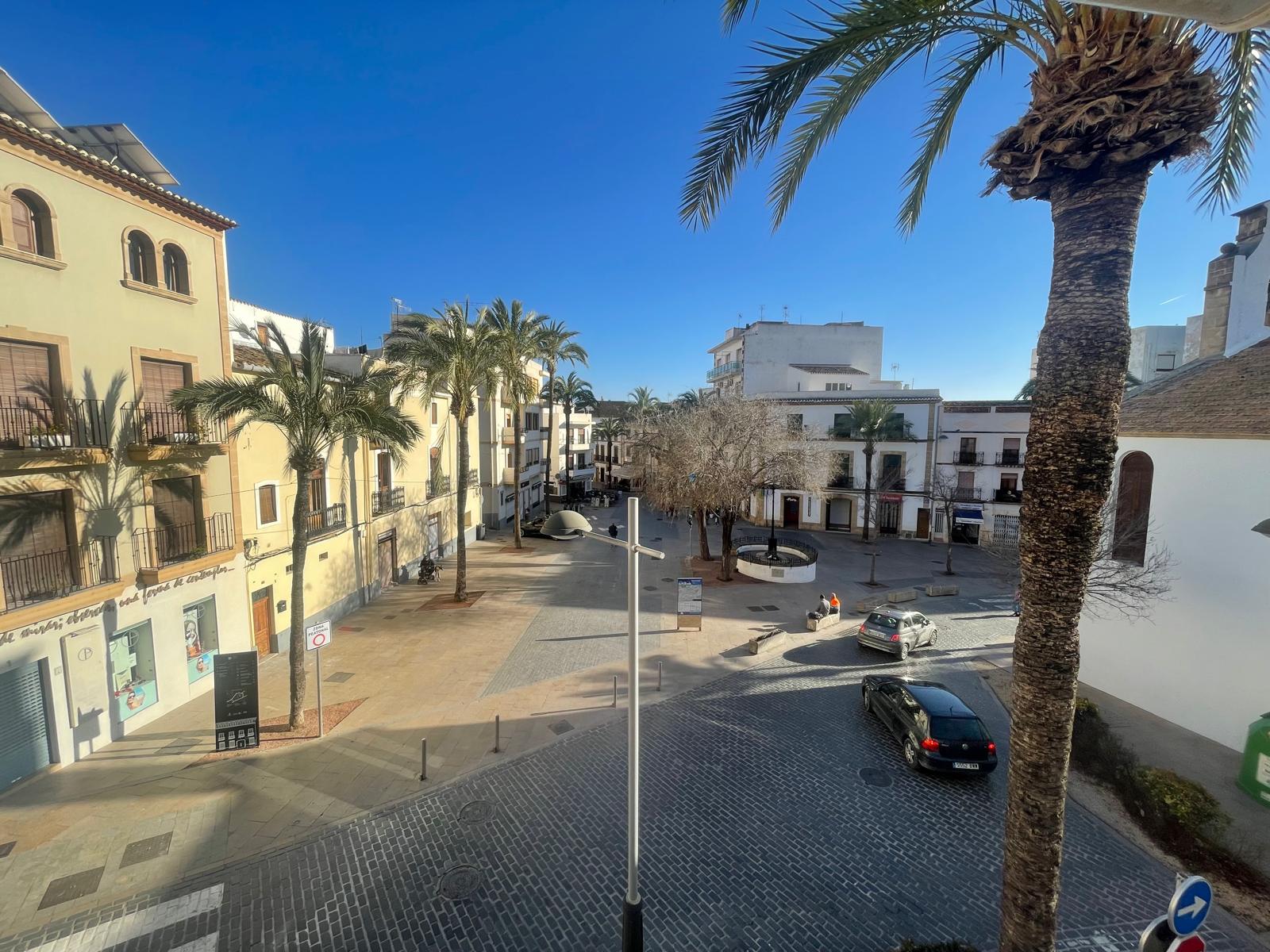 Elevated view from the property overlooking a cobblestone square in Jávea's old town, featuring traditional Mediterranean buildings and mature palm trees.