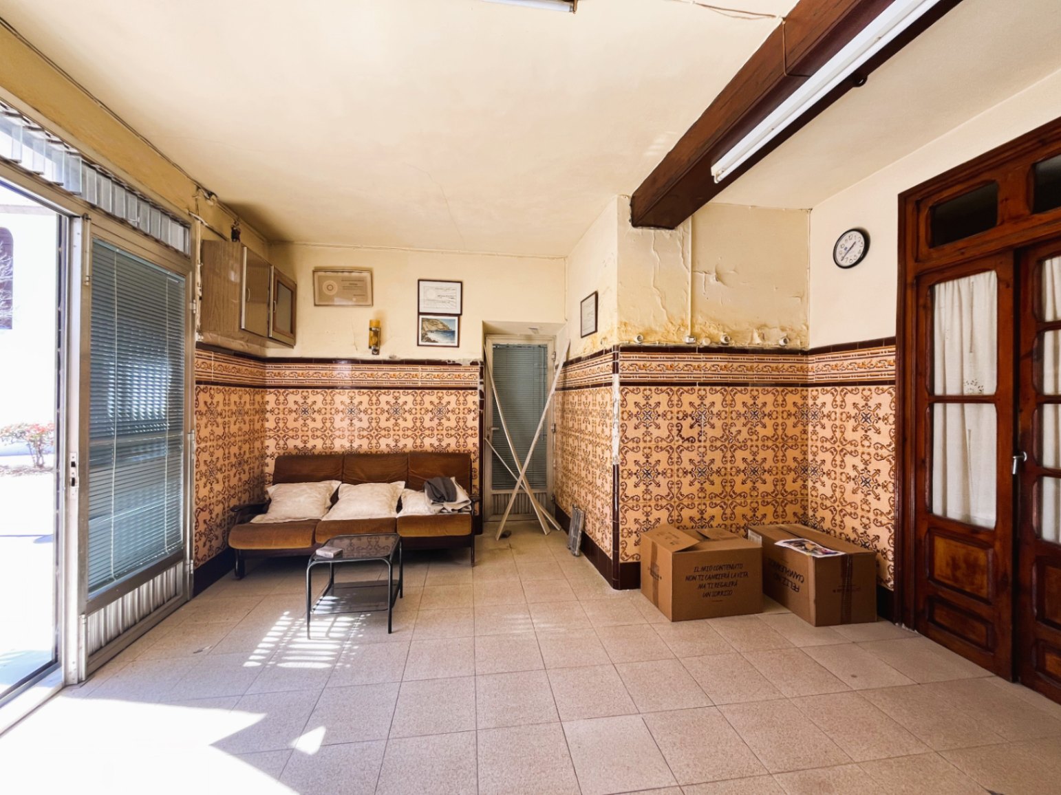 Entrance living area featuring traditional patterned wall tiles, an exposed wooden beam, and a large glass door providing extensive natural light.