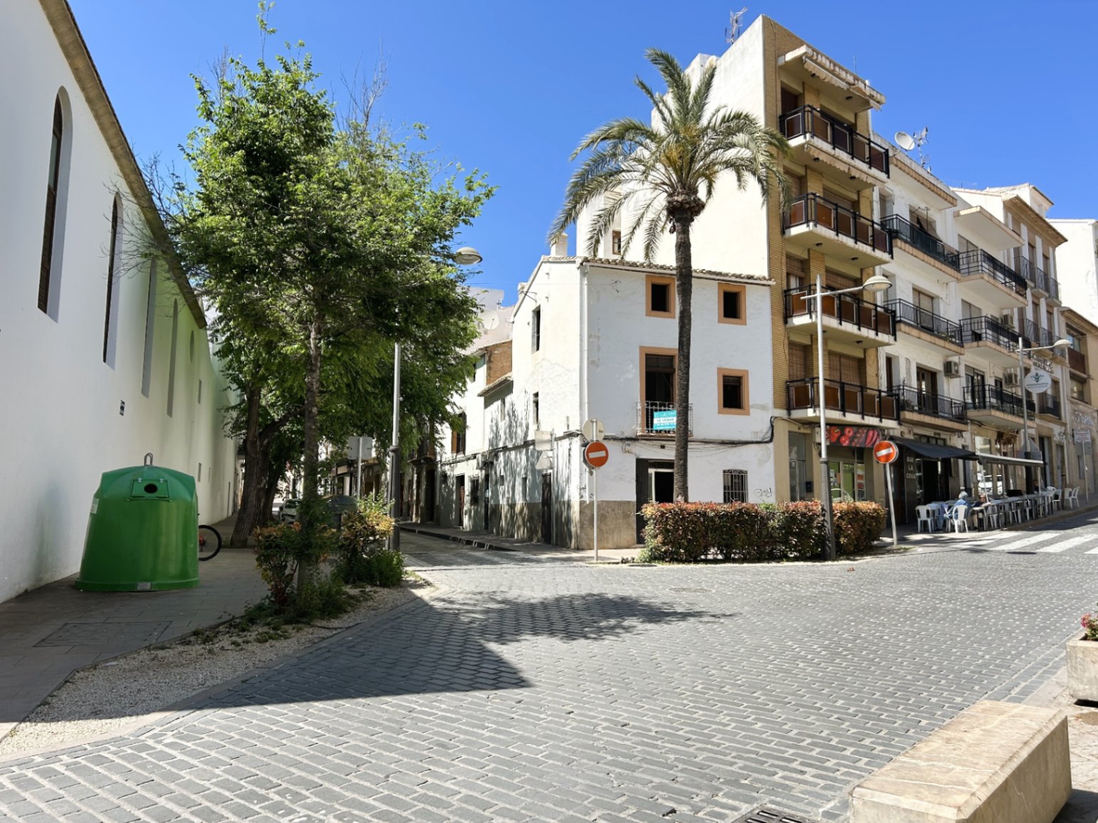 Exterior view of the white corner townhouse facade located on a cobbled street in Jávea's historic center, featuring a palm tree and traditional architecture.