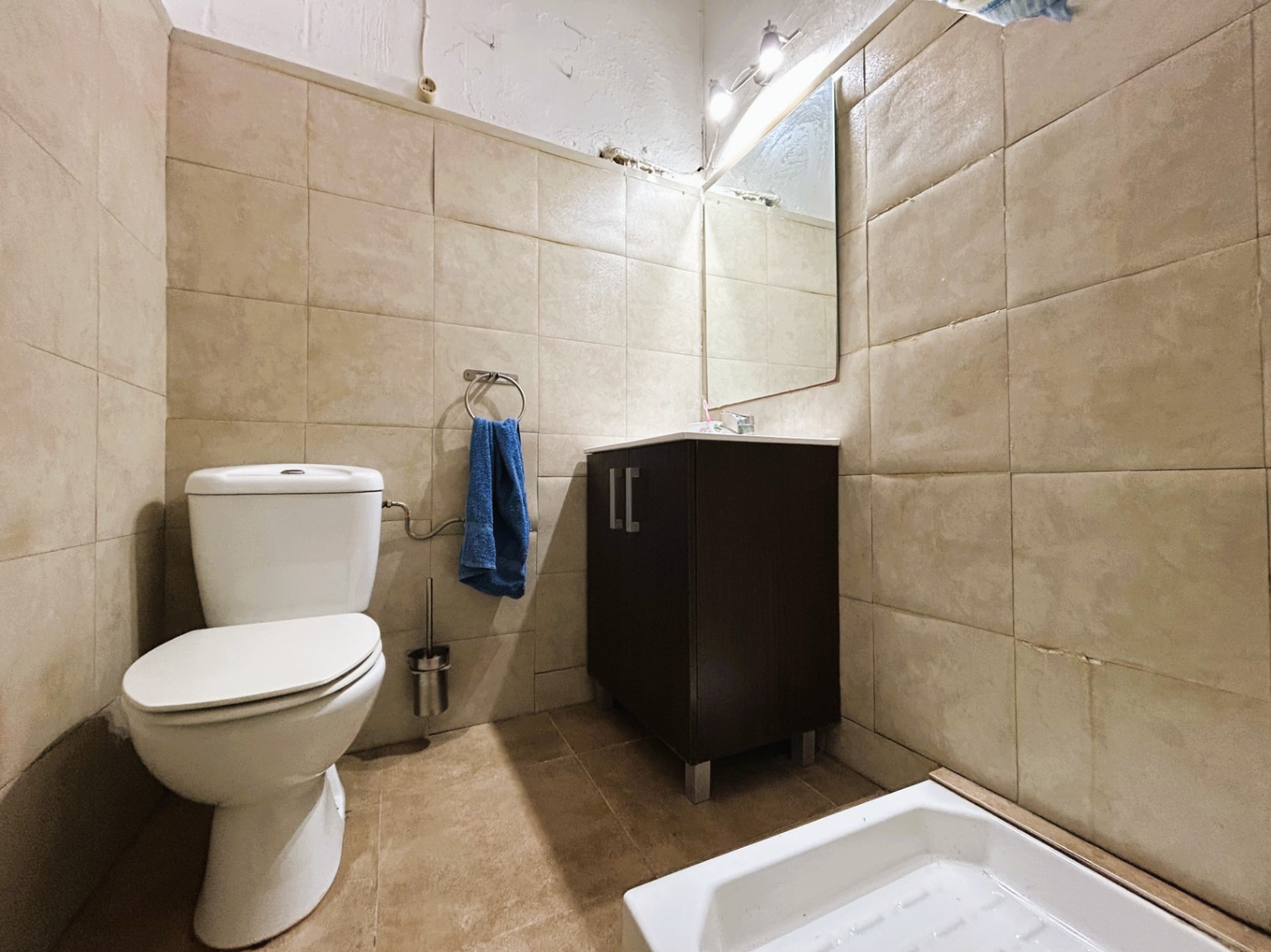 Functional bathroom featuring beige tiled walls, a white ceramic toilet, and a dark wood vanity unit with an integrated mirror and lighting.