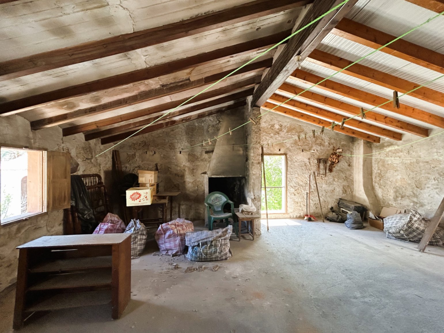 Spacious attic featuring exposed wooden beams, original stone walls, and an open fireplace, providing significant renovation potential in the historic center.