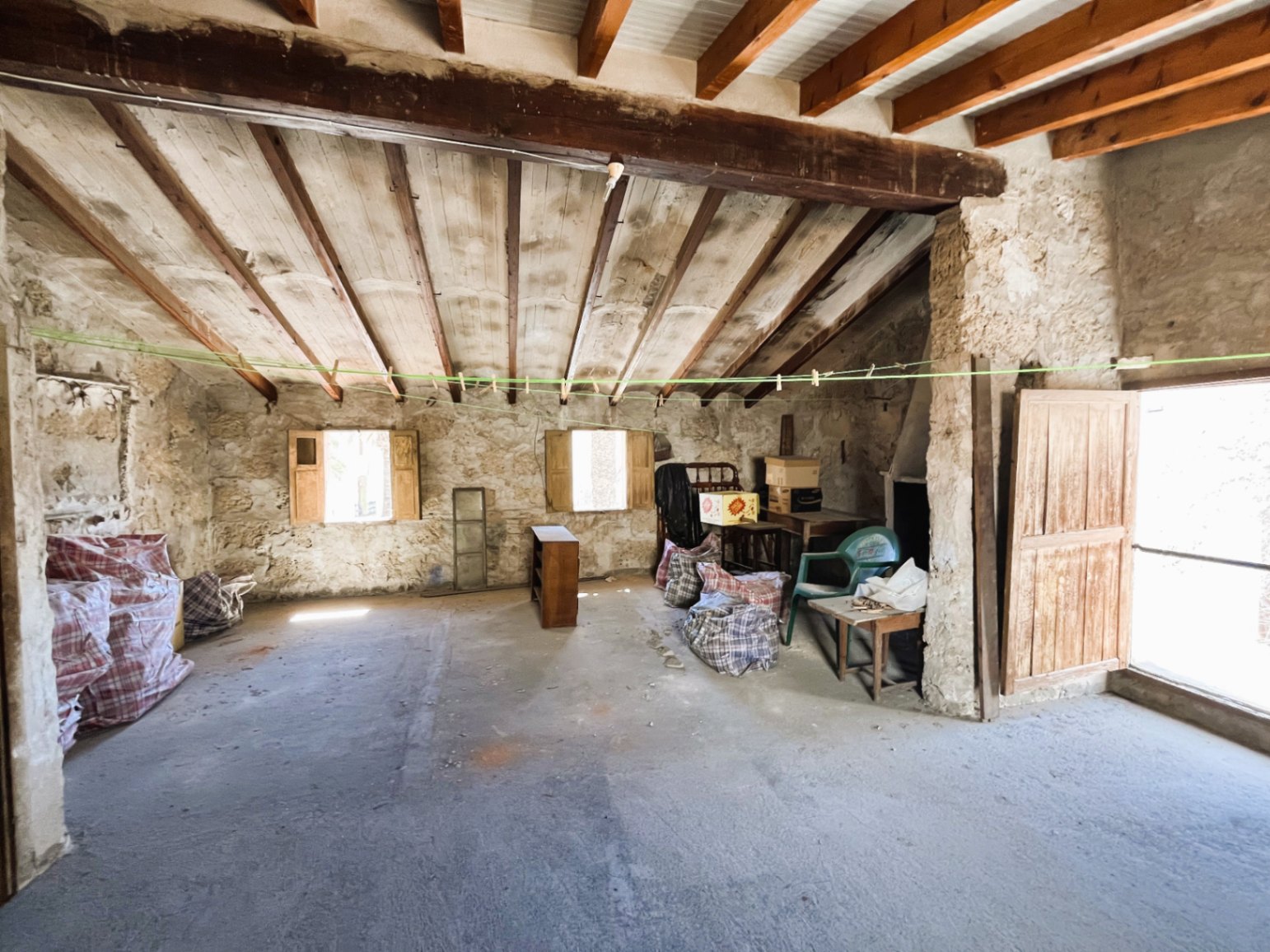 Spacious attic with exposed wooden beams and natural stone walls, featuring a traditional sloped roof structure with significant potential for a full renovation.