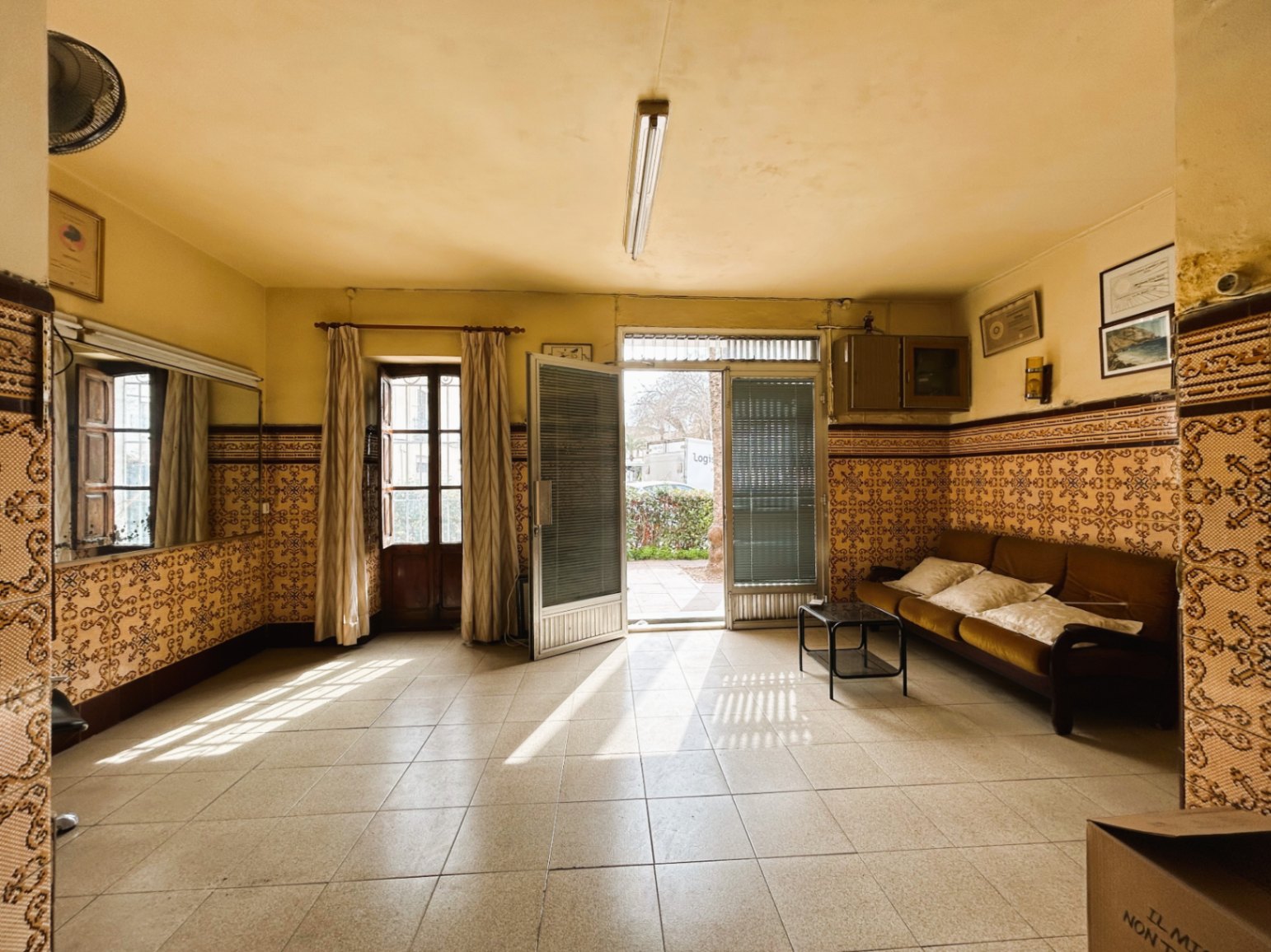 Spacious entrance hall featuring traditional patterned wall tiles, ceramic flooring, and large doors opening to the outside, providing ample natural light.