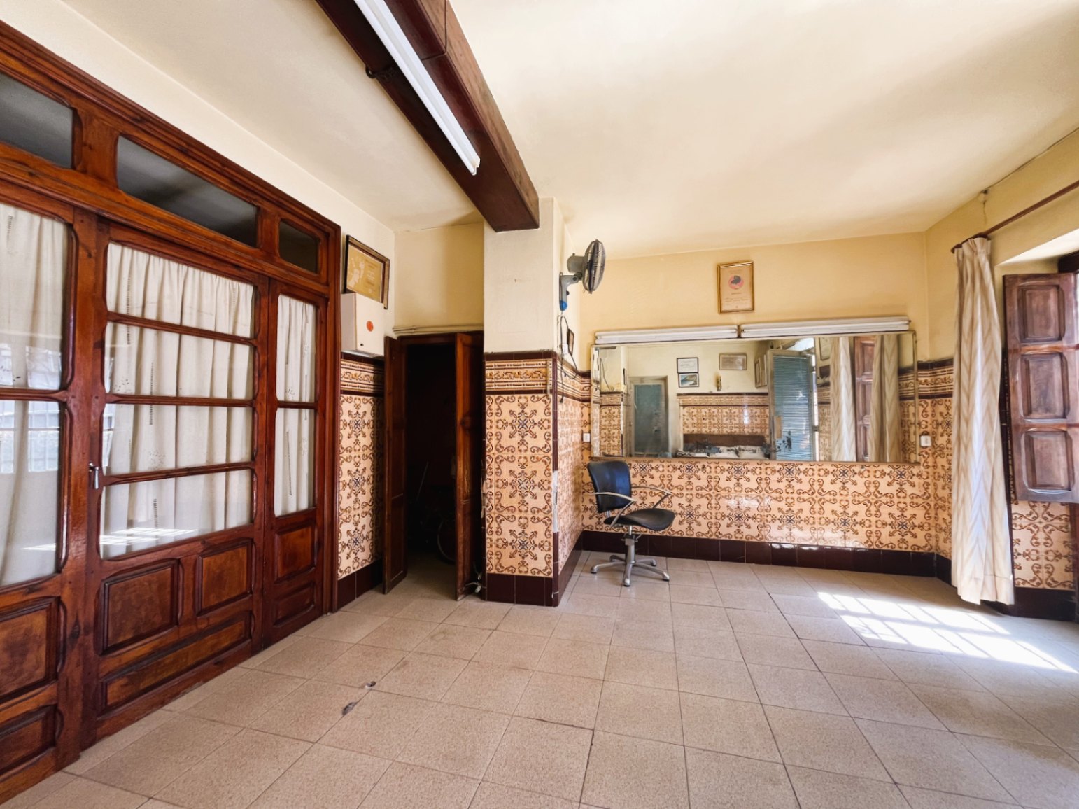 Spacious room featuring traditional patterned wall tiles, exposed dark wooden beams, and large glass-paneled doors with classic woodwork.
