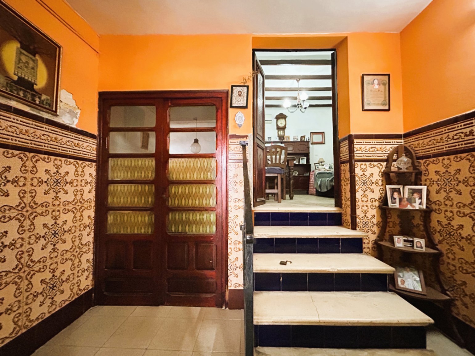 Traditional entrance featuring ornate ceramic wall tiles, terracotta walls, and a marble staircase with blue risers leading to a room with exposed wooden beams.