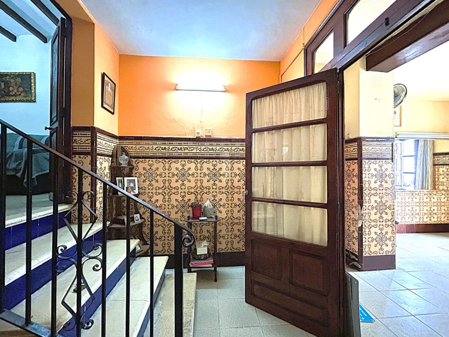 Traditional entrance hall featuring decorative wall tiles, a stone staircase with blue risers, and a classic wrought iron railing in Jávea's old town.