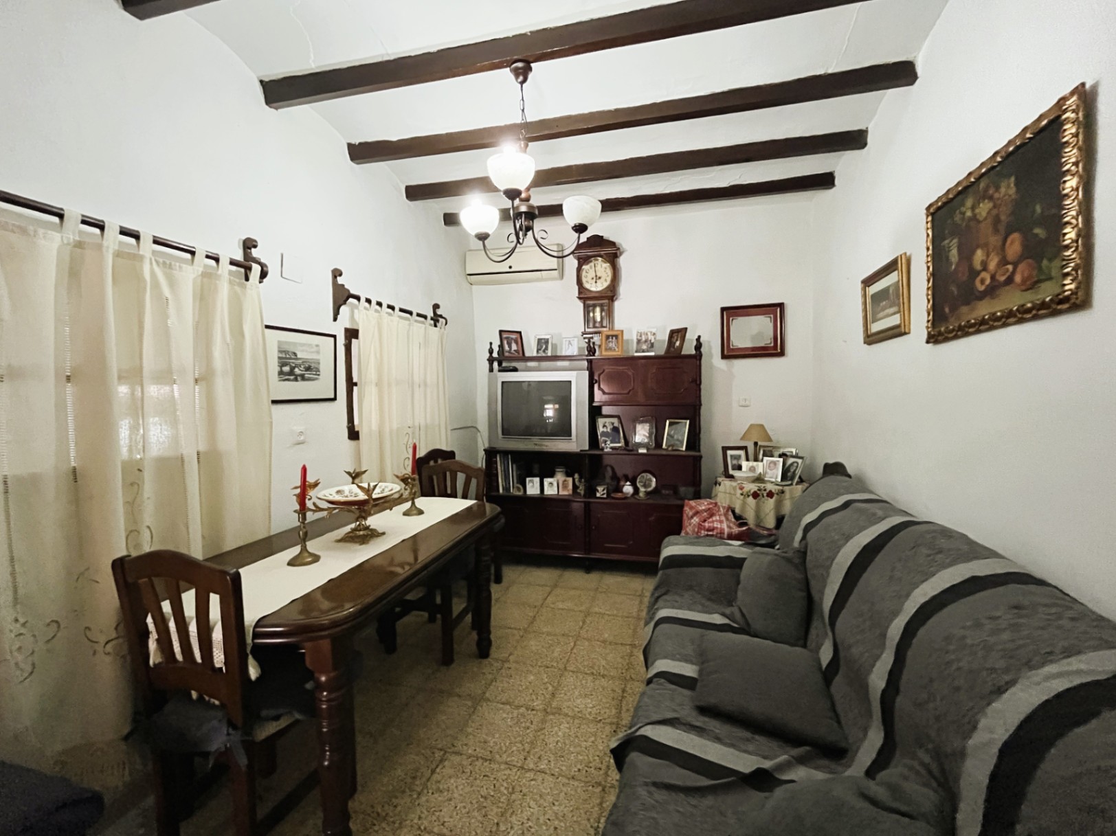 Traditional living-dining area featuring exposed dark wood ceiling beams, terrazzo flooring, and classic dark wood furniture in Jávea's historic center.