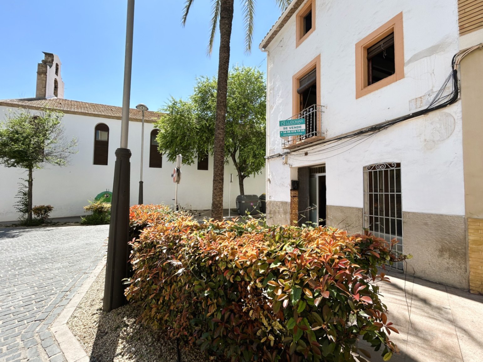 Traditional white facade with ochre window frames, located on a cobblestone plaza adjacent to a historic church in Jávea's old town.