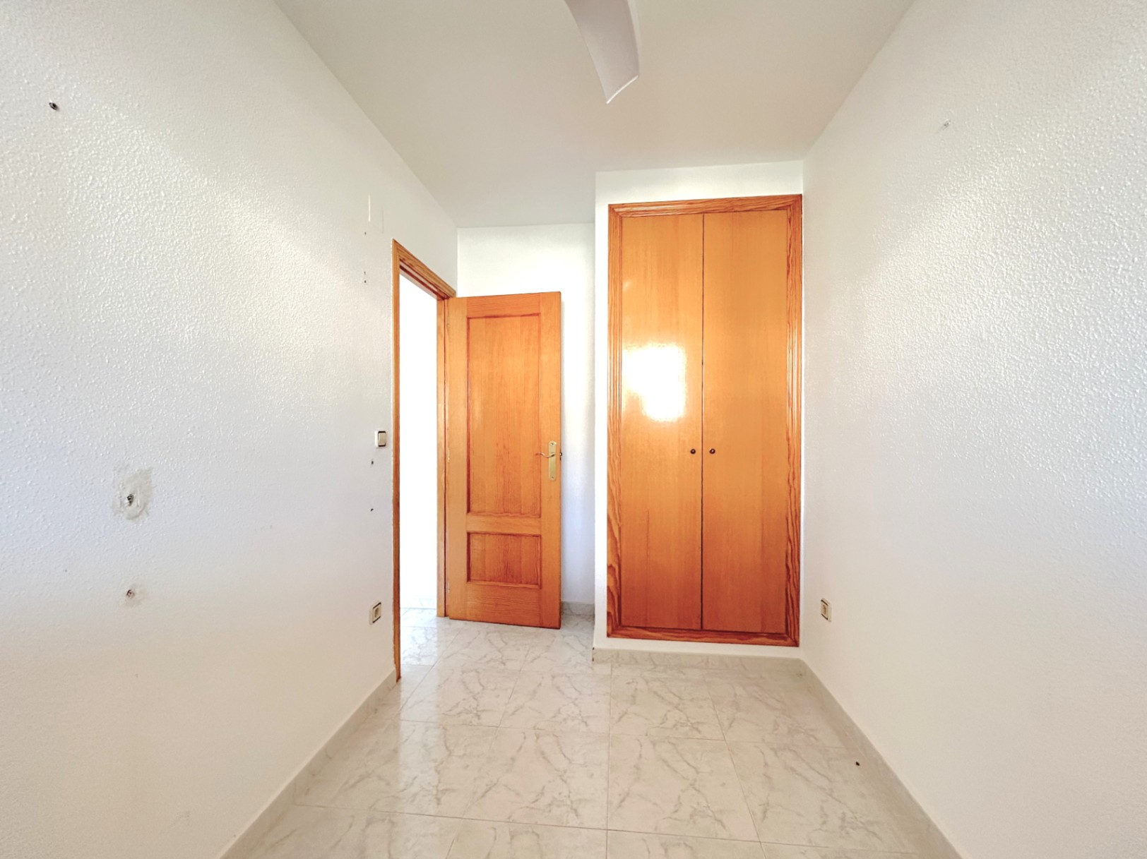 Distribution hallway featuring marble-effect ceramic flooring, white walls, and a built-in natural wood wardrobe with matching door.