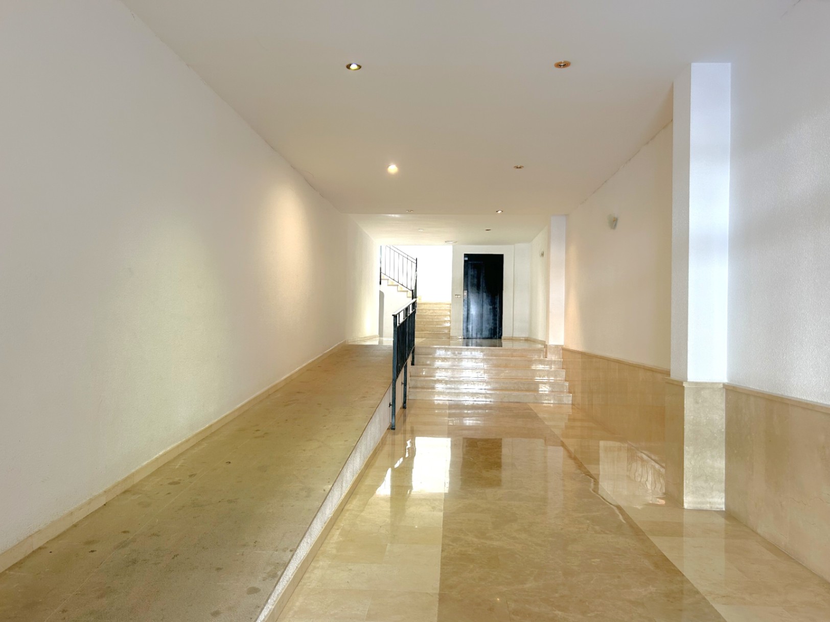 Entrance hall featuring polished marble flooring, an accessibility ramp with metal railing, recessed ceiling lighting, and clean white walls.