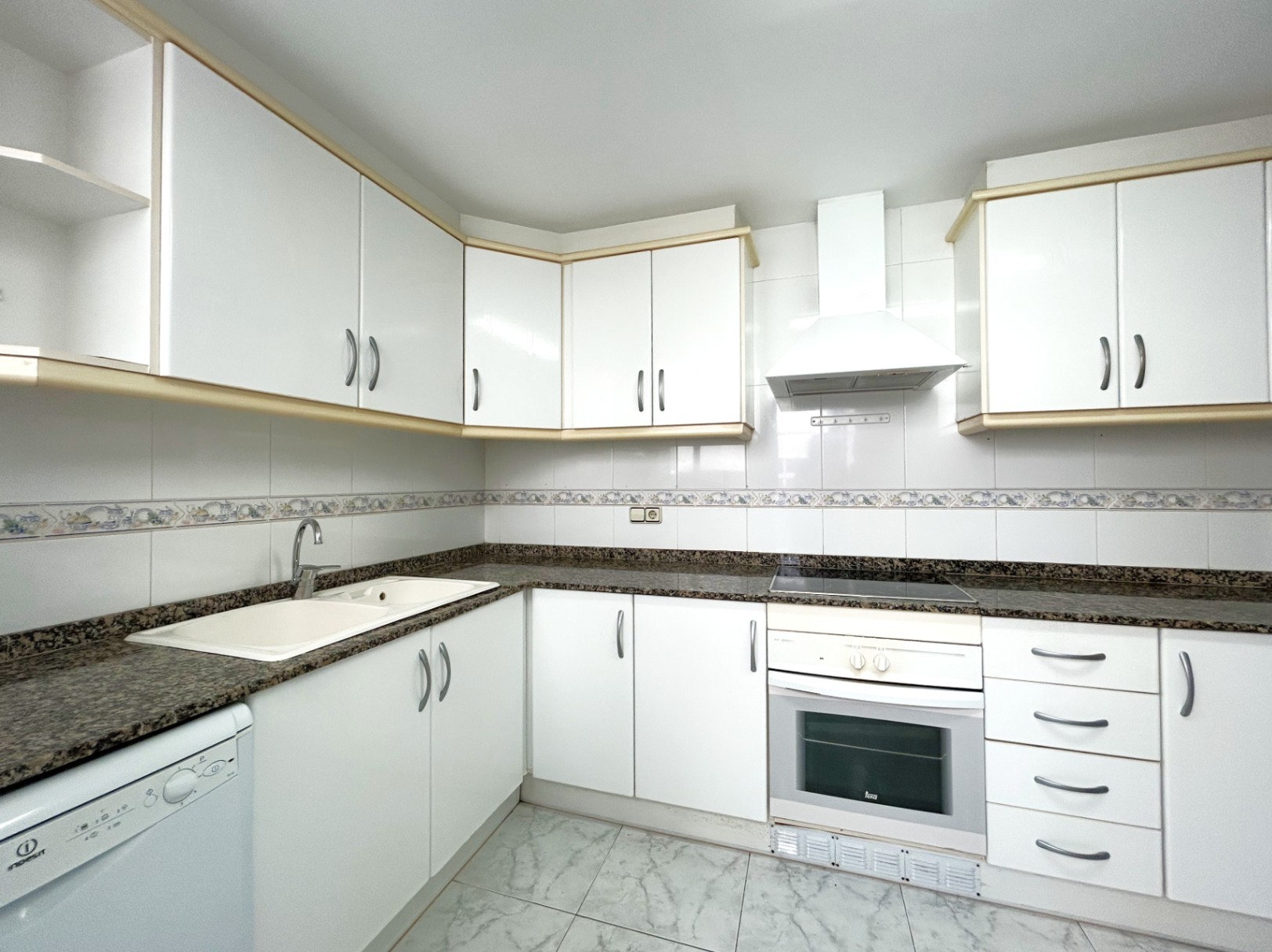 Independent kitchen featuring white cabinetry with wood trim, granite countertops, an electric hob, and a built-in oven. The walls are tiled with a decorative border.