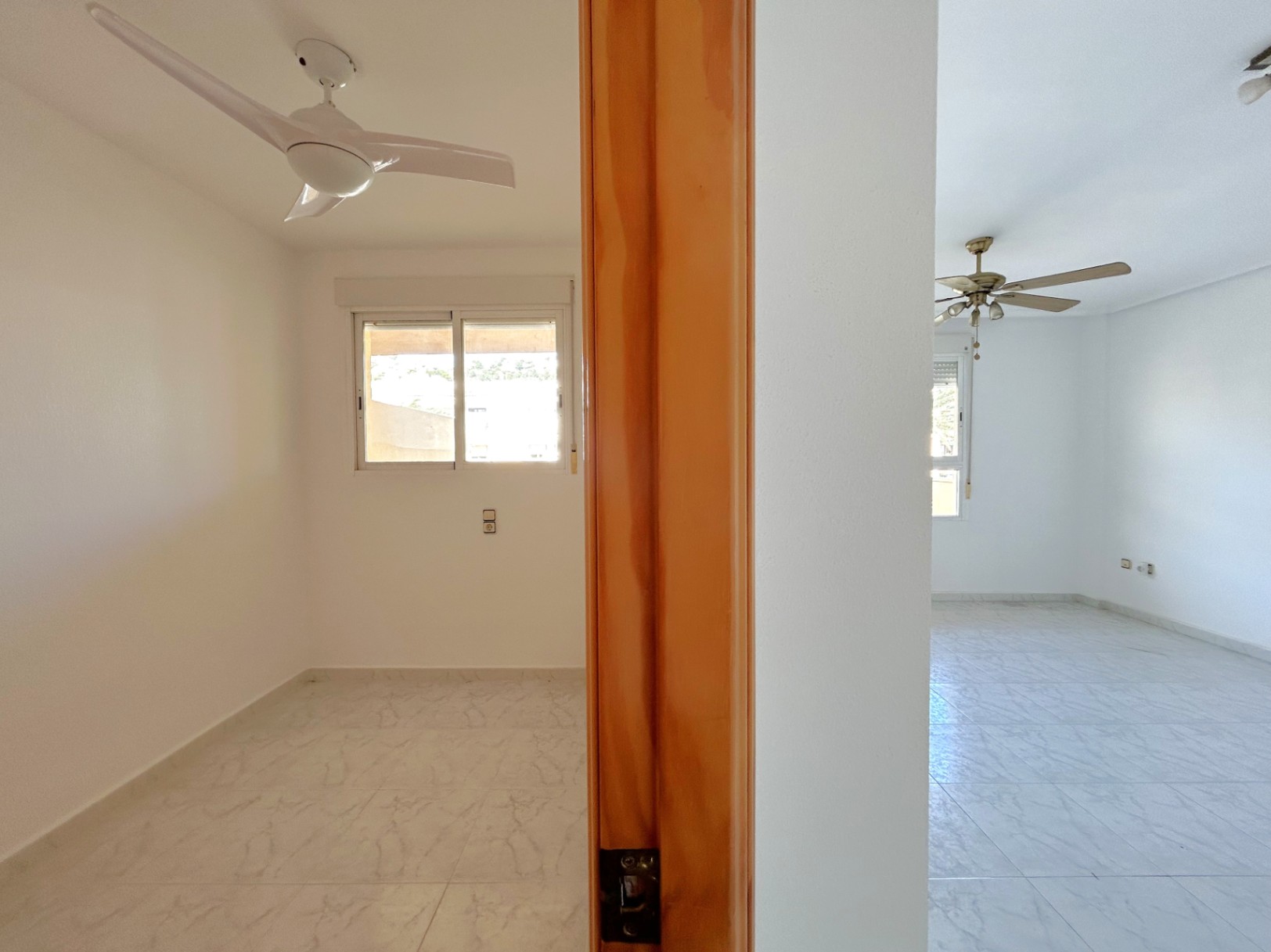 Interior view of two adjacent bedrooms featuring tiled floors, ceiling fans, and natural wood door frames.