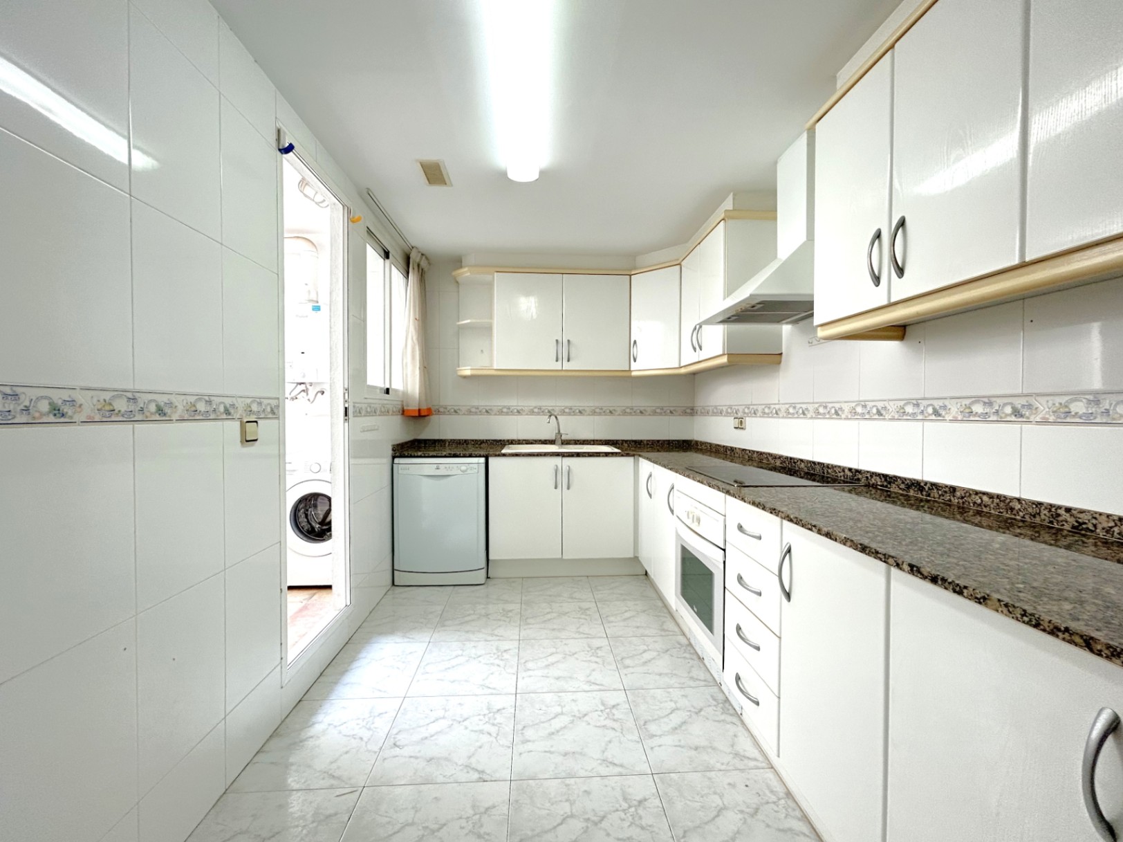 L-shaped independent kitchen featuring white cabinetry with wood trim, dark granite countertops, and a doorway leading to a utility laundry area.