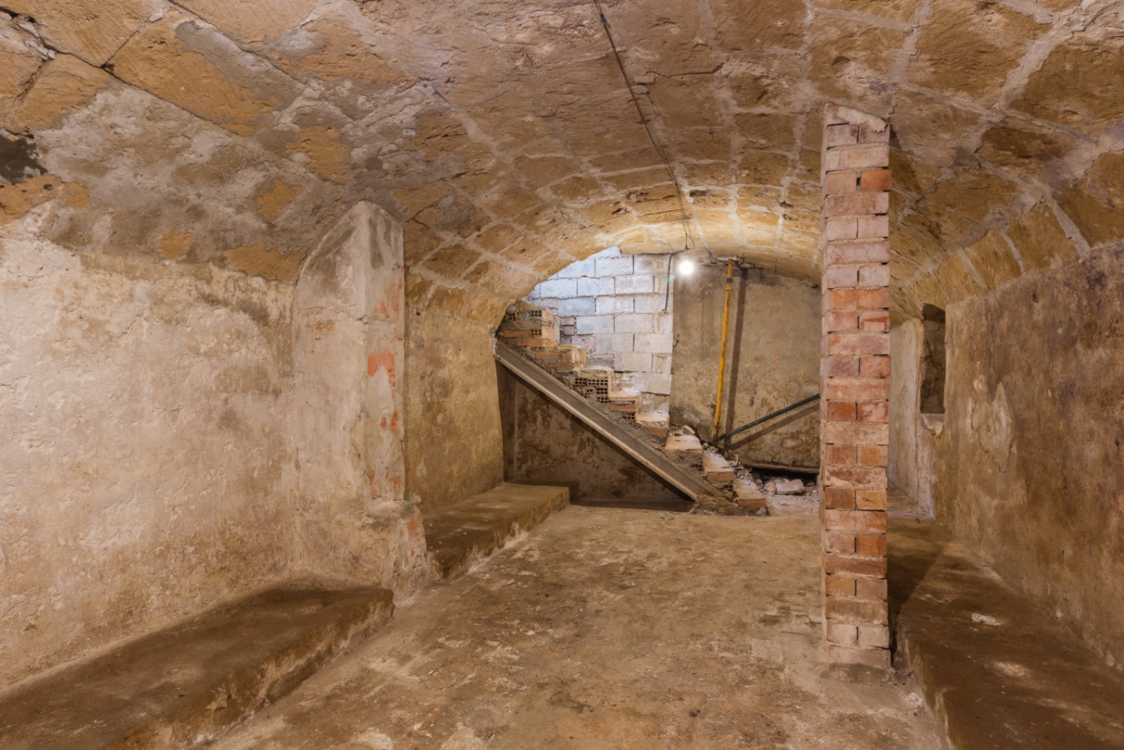 Basement featuring original vaulted tosca stone ceilings and an exposed brick pillar. This rustic space includes a staircase area and offers potential for a cellar.