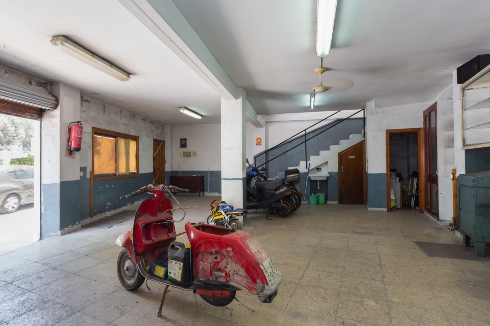 Open-plan main floor featuring ceramic tiling, a metal roll-up entrance, and a staircase leading to the upper level. Versatile space with fluorescent lighting.