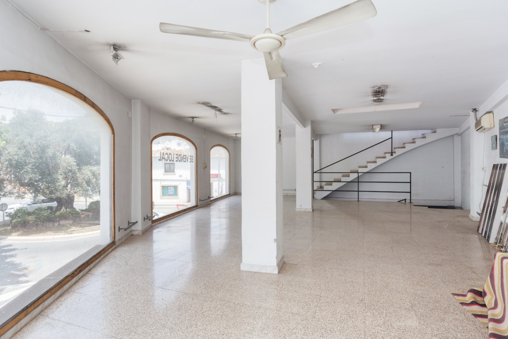 Open-plan main floor featuring large arched windows, terrazzo flooring, and a staircase with a black metal railing leading to the upper level.