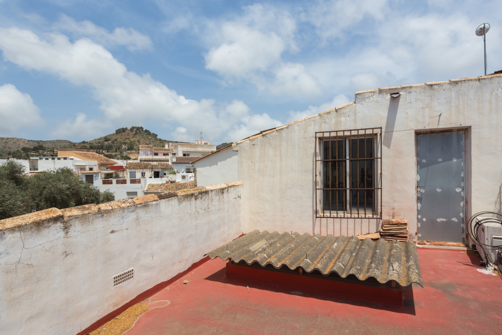 Rooftop terrace featuring a red-painted floor and panoramic views of the surrounding town and hills. The space includes a gated window and direct access.