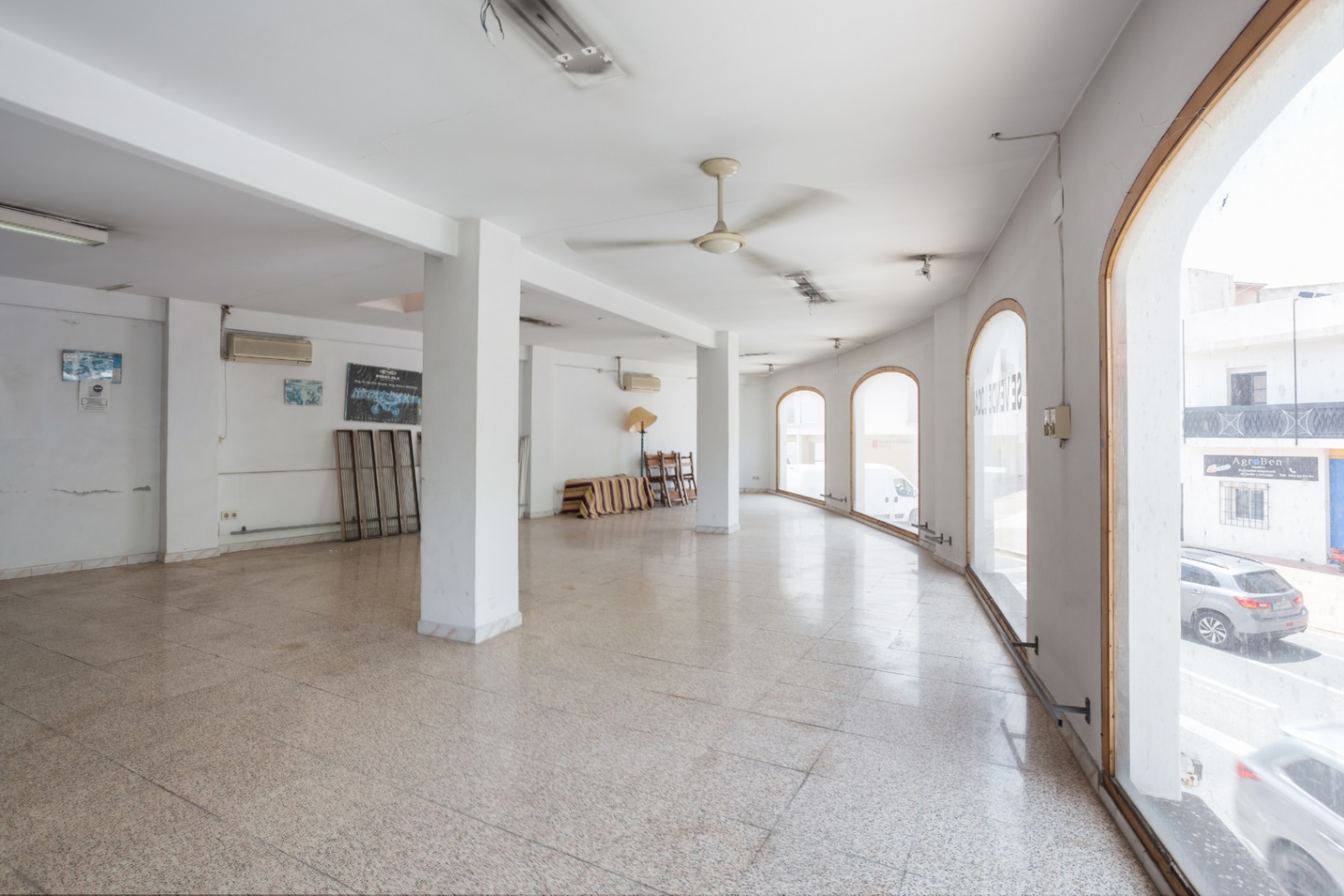 Spacious open-plan commercial area featuring large arched windows, polished terrazzo flooring, and white structural columns for a bright atmosphere.