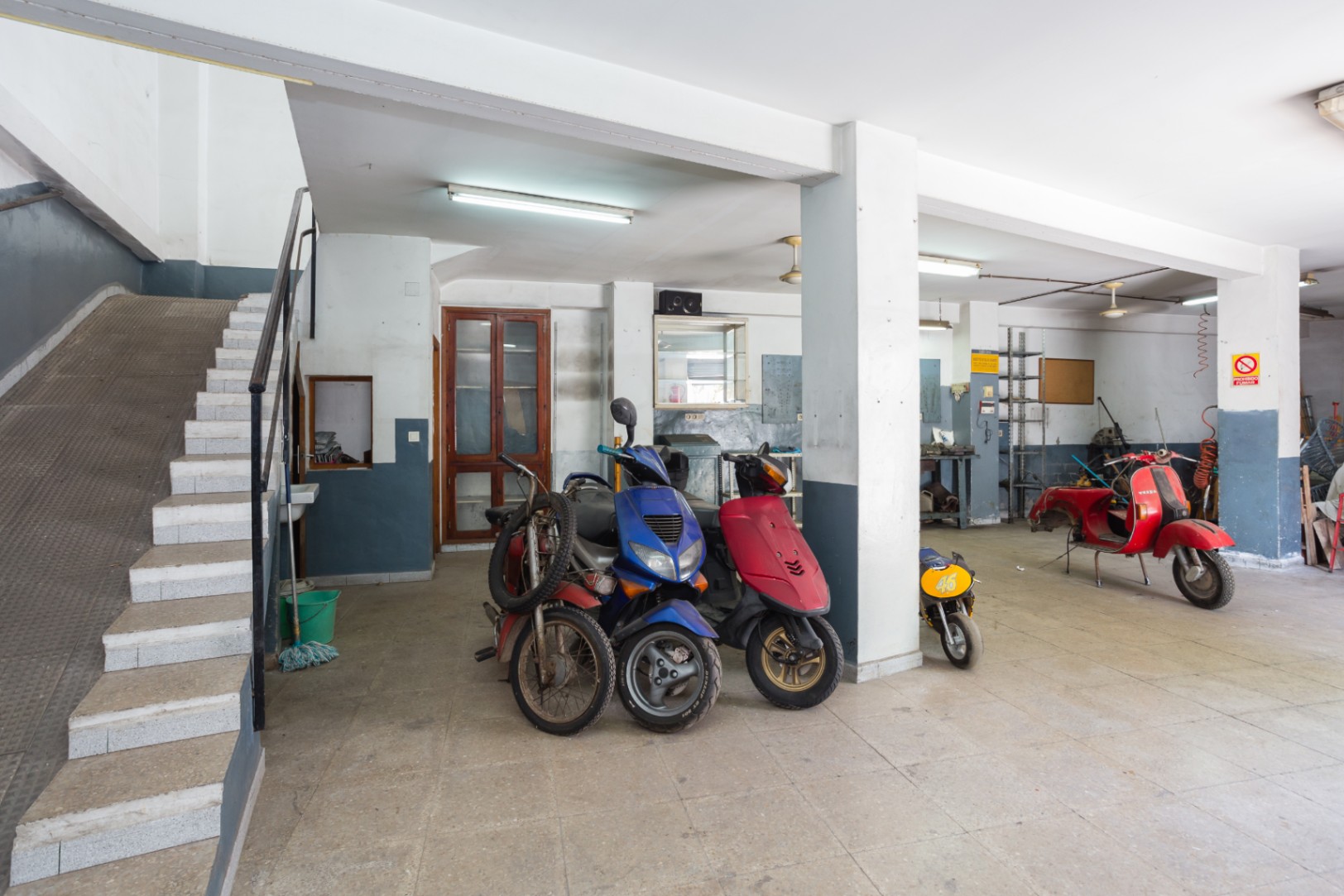 Spacious open-plan garage or workshop area featuring structural pillars, fluorescent lighting, and access via both stairs and a side ramp.