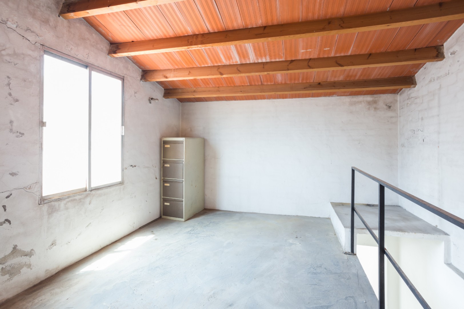 Upper floor featuring exposed wooden beams, clay tile ceiling, concrete flooring, and a large window providing ample natural light.