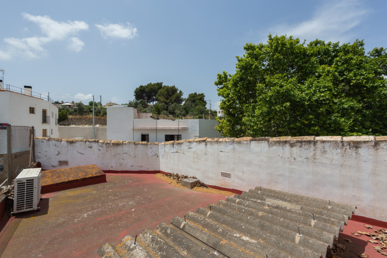 Upper roof terrace featuring red flooring and white masonry walls, providing open views of the surrounding neighborhood and mature trees.