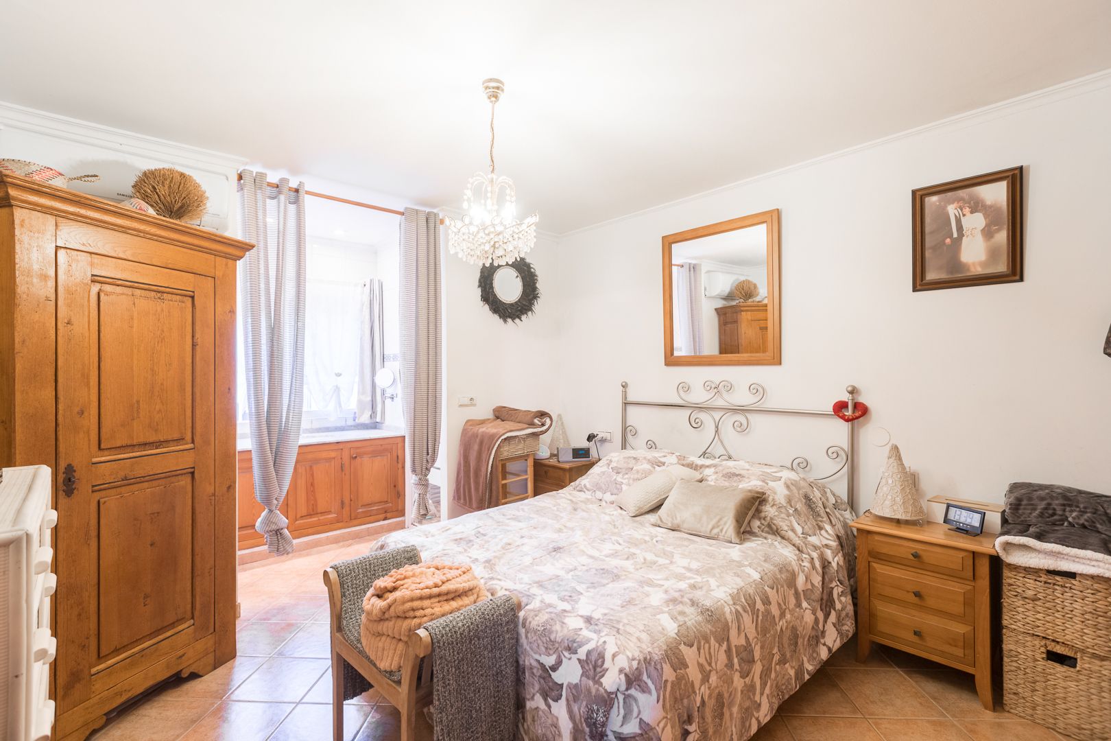 Bedroom featuring ceramic tile floors, a classic wooden wardrobe, and a wrought iron headboard. Includes air conditioning, a crystal chandelier, and natural light.