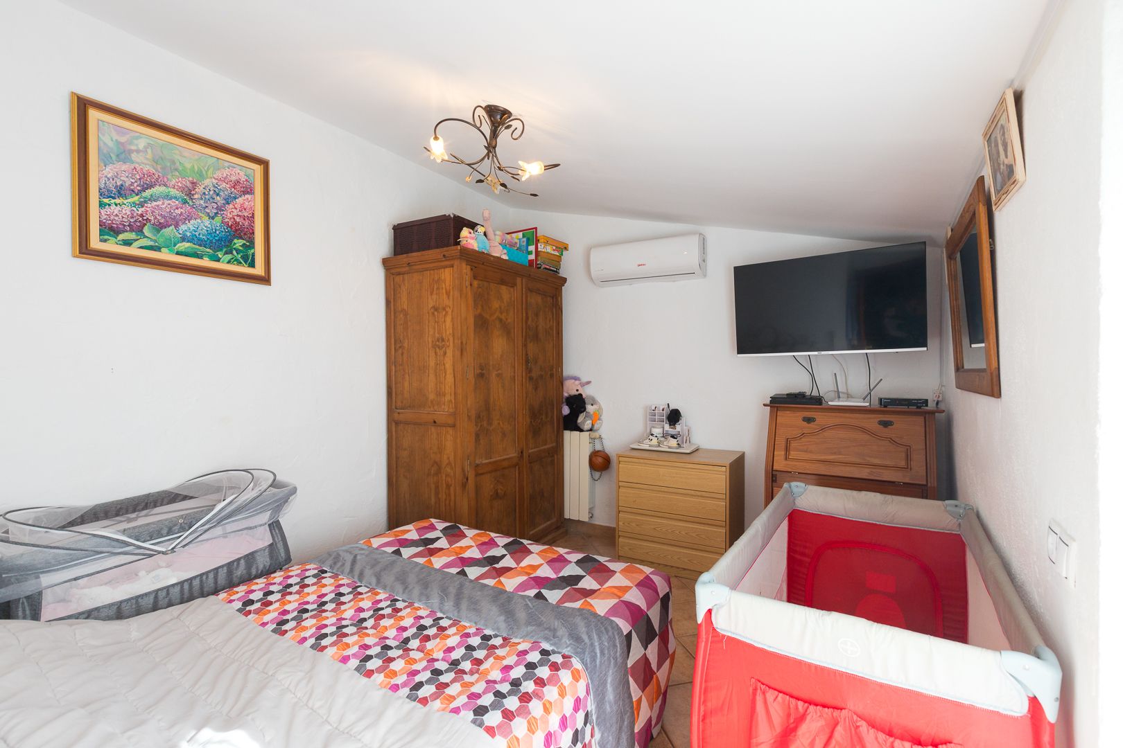 Bright bedroom featuring sloped ceilings, air conditioning, classic wooden furniture, and a functional layout suitable for family needs.