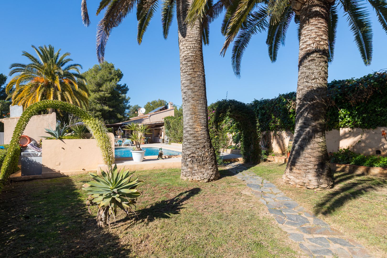 Mediterranean garden featuring mature palm trees, a natural stone path, and a view of the swimming pool and villa.
