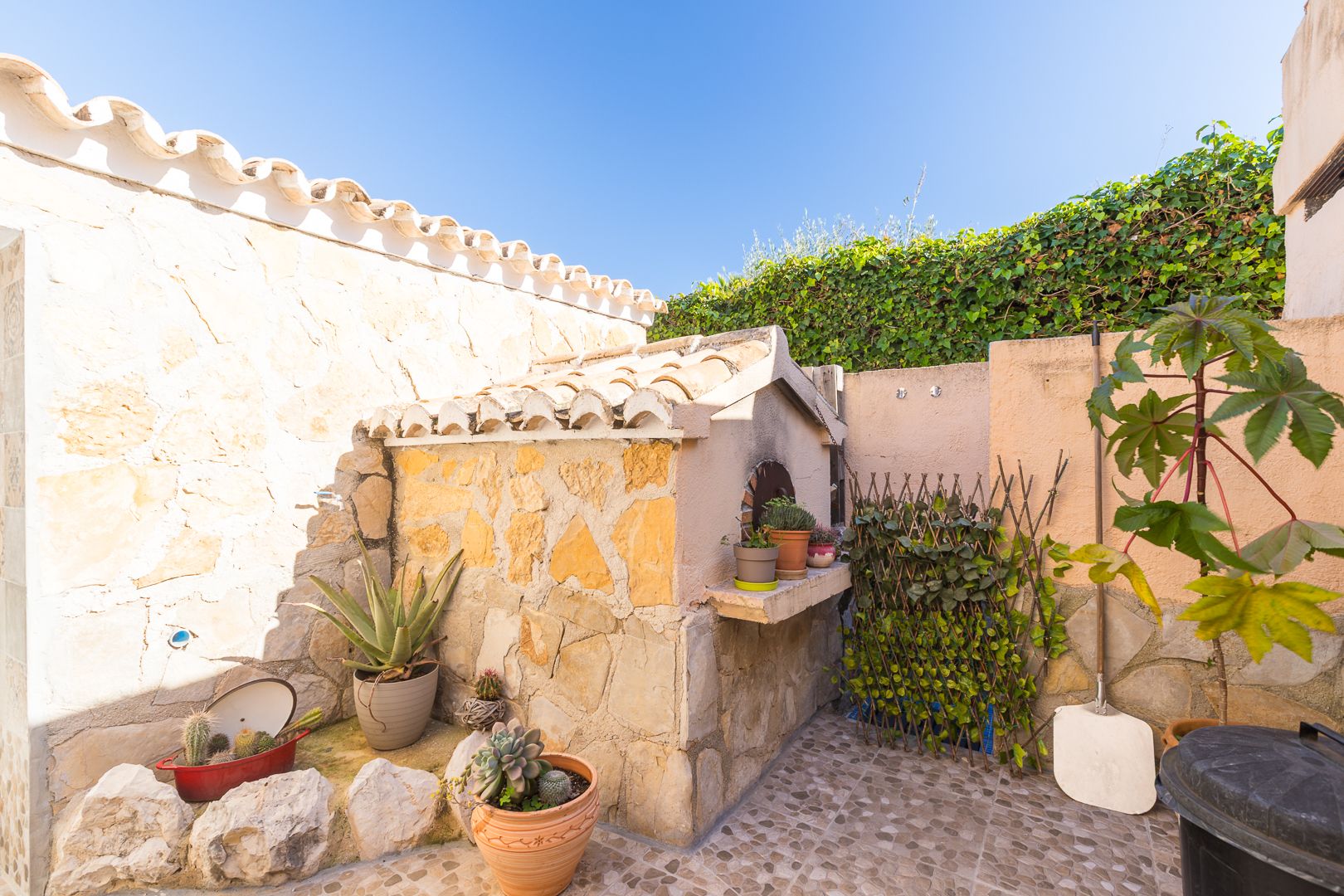 Traditional wood-fired oven built with natural stone and a terracotta tile roof, featuring an outdoor patio with succulents and a Mediterranean aesthetic.