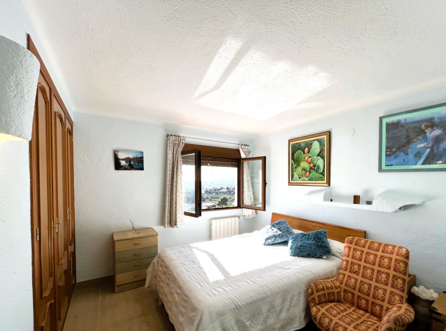 Bedroom featuring built-in wooden wardrobes and a double bed, with an open window providing natural light and views of the surrounding landscape.