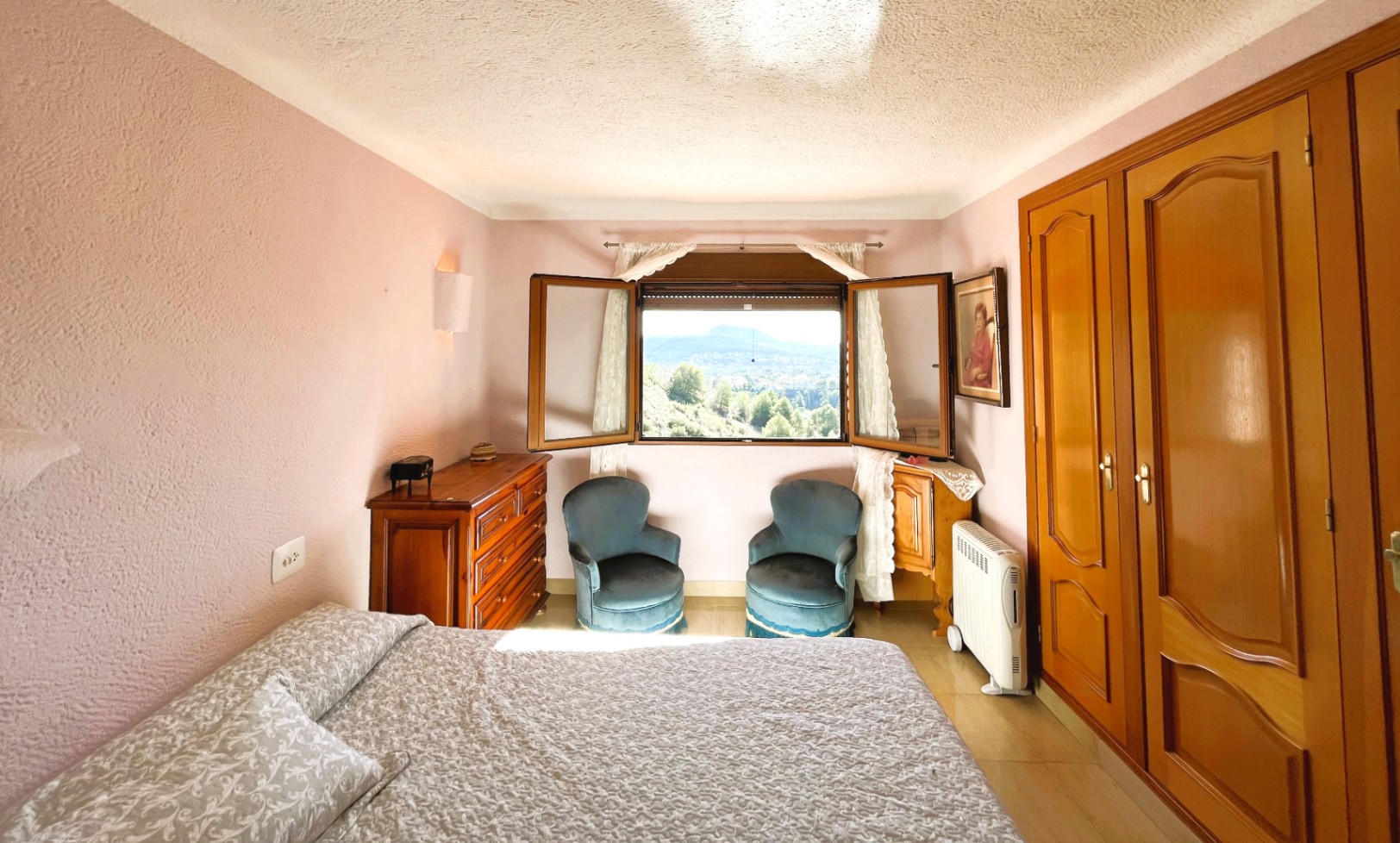 Bedroom featuring mauve textured walls, built-in wooden wardrobes, and a central window showcasing panoramic views of the valley and mountains.