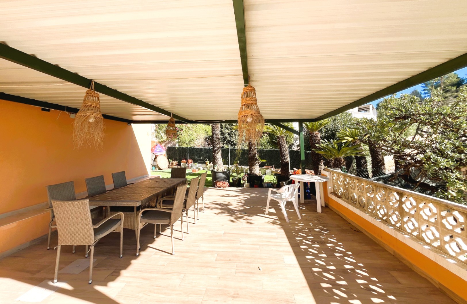 Covered terrace featuring an outdoor dining area with wicker chairs, decorative pendant lights, and views over the landscaped garden.