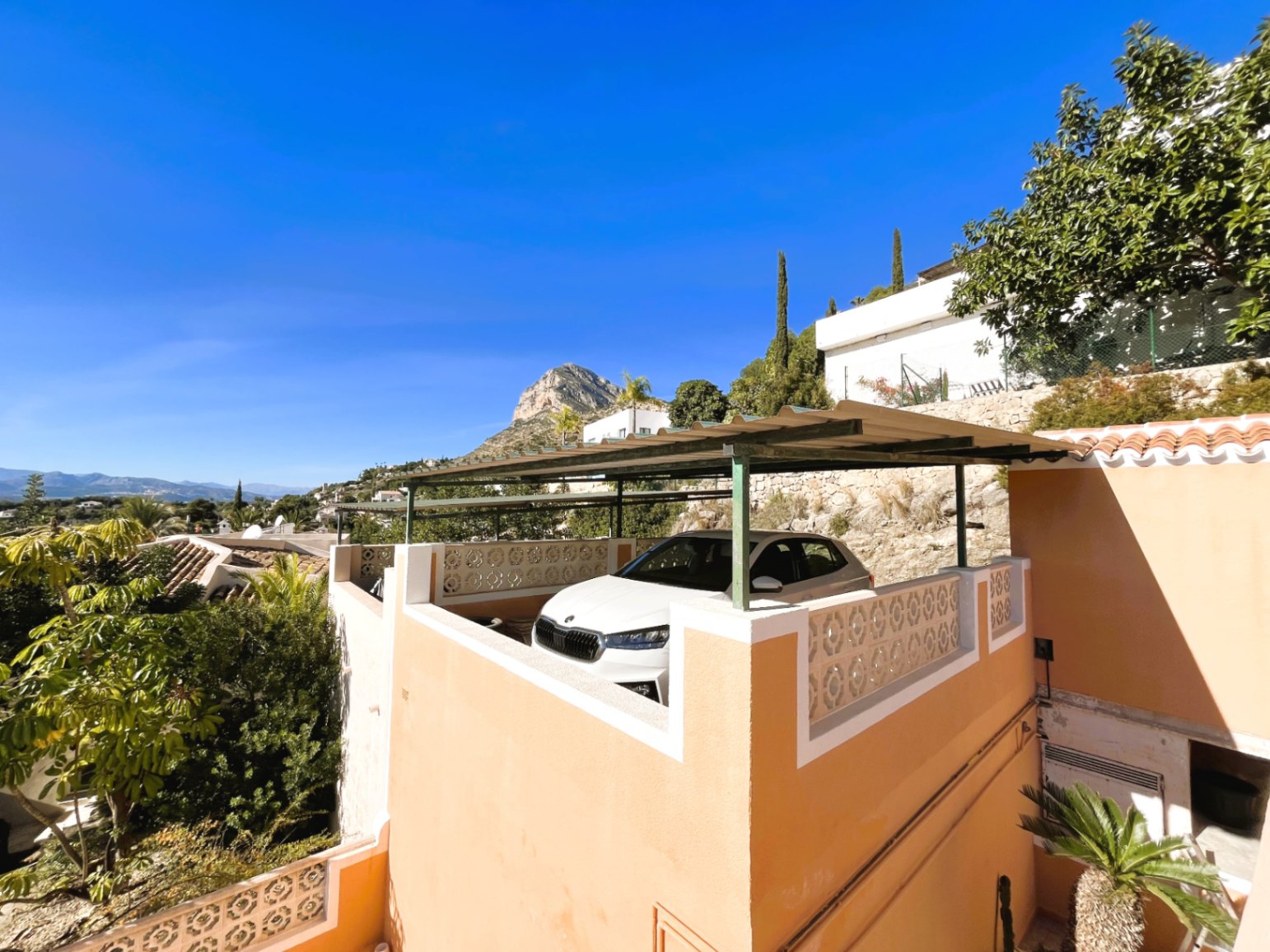 Elevated parking area featuring a metal pergola and decorative lattice railing, providing direct views of the Montgó mountain and lush vegetation.