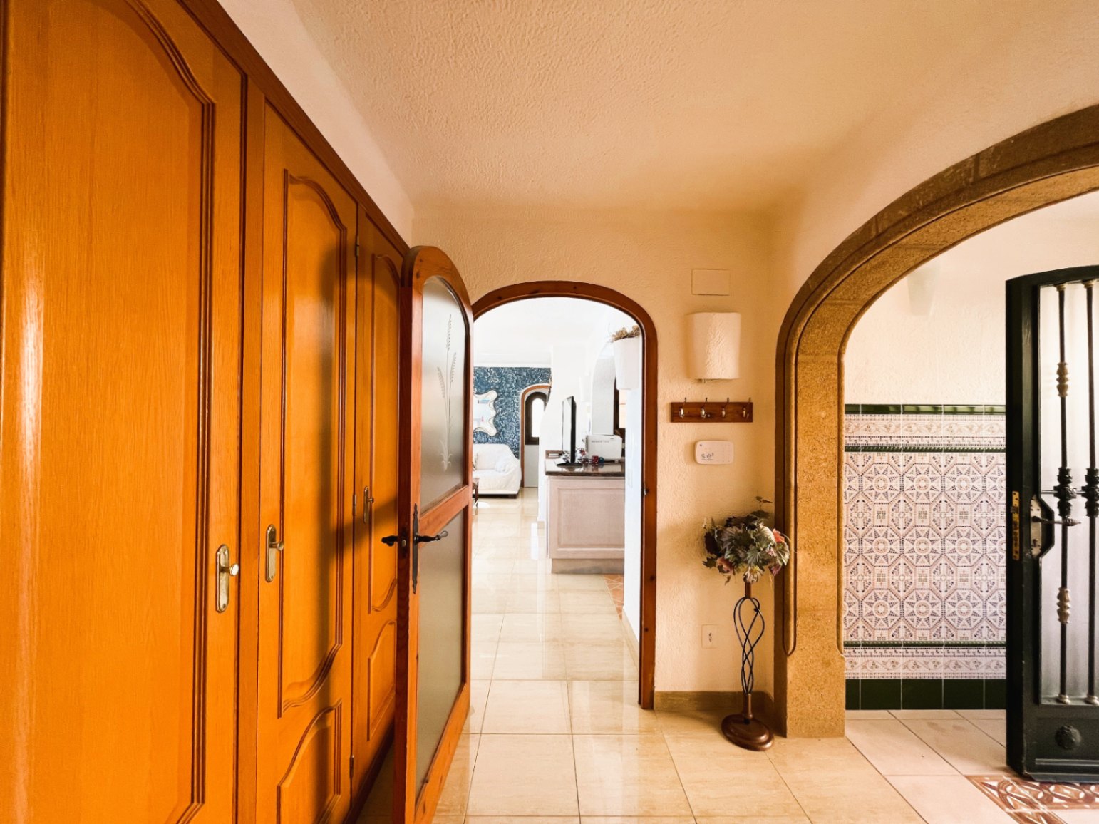Entrance hallway featuring built-in wooden wardrobes, polished tile flooring, and arched transitions leading to the living area and a traditional tiled alcove.
