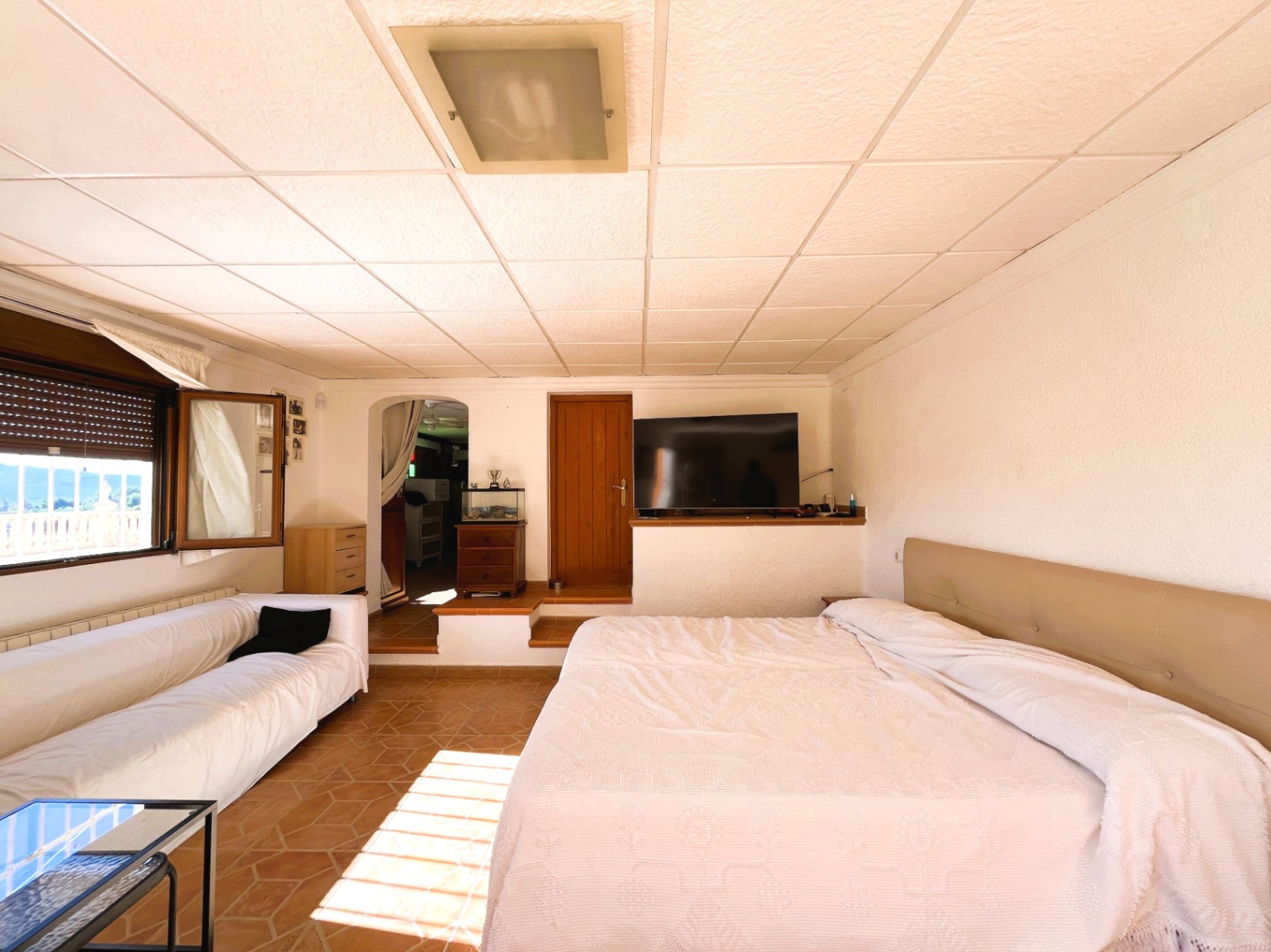 Lower-level bedroom featuring terracotta flooring, an integrated lounge area, and natural light with views of the surrounding landscape.