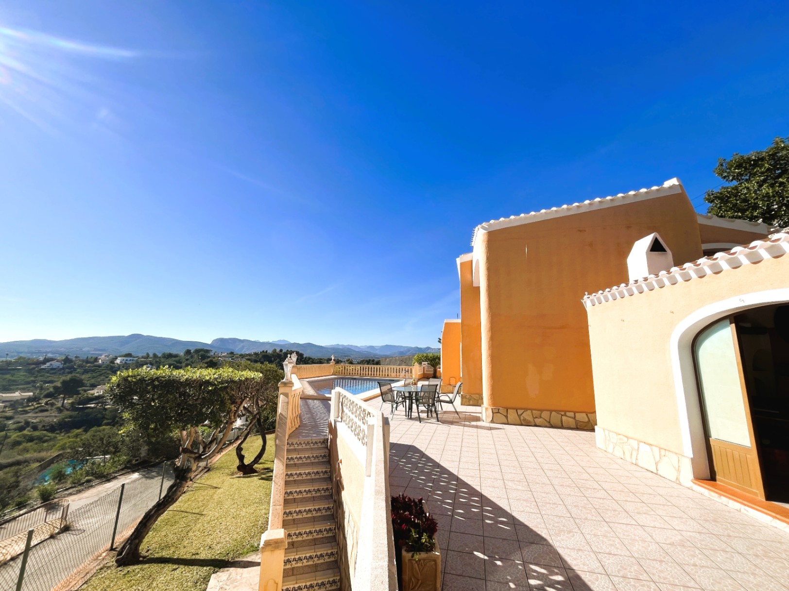 South-facing main terrace featuring an outdoor dining area and panoramic mountain views. The space connects the villa to the private pool and landscaped surroundings.