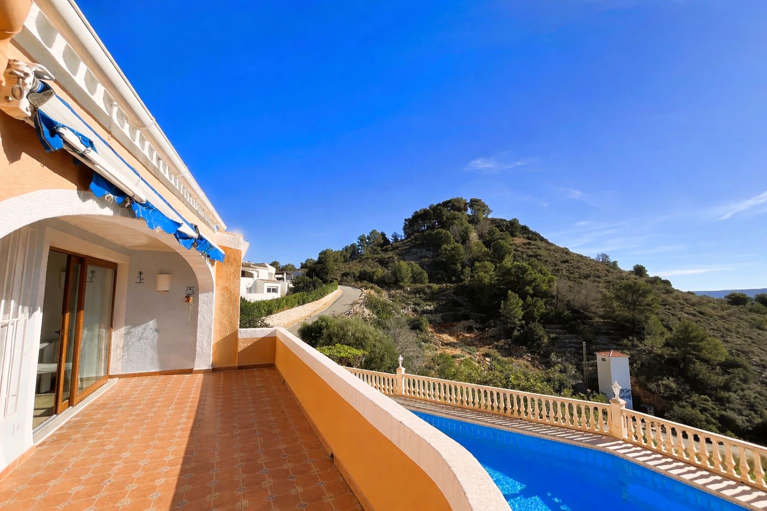 Upper terrace featuring terracotta tiling, a retractable awning, and panoramic views of the Montgó hillside and the private pool below.