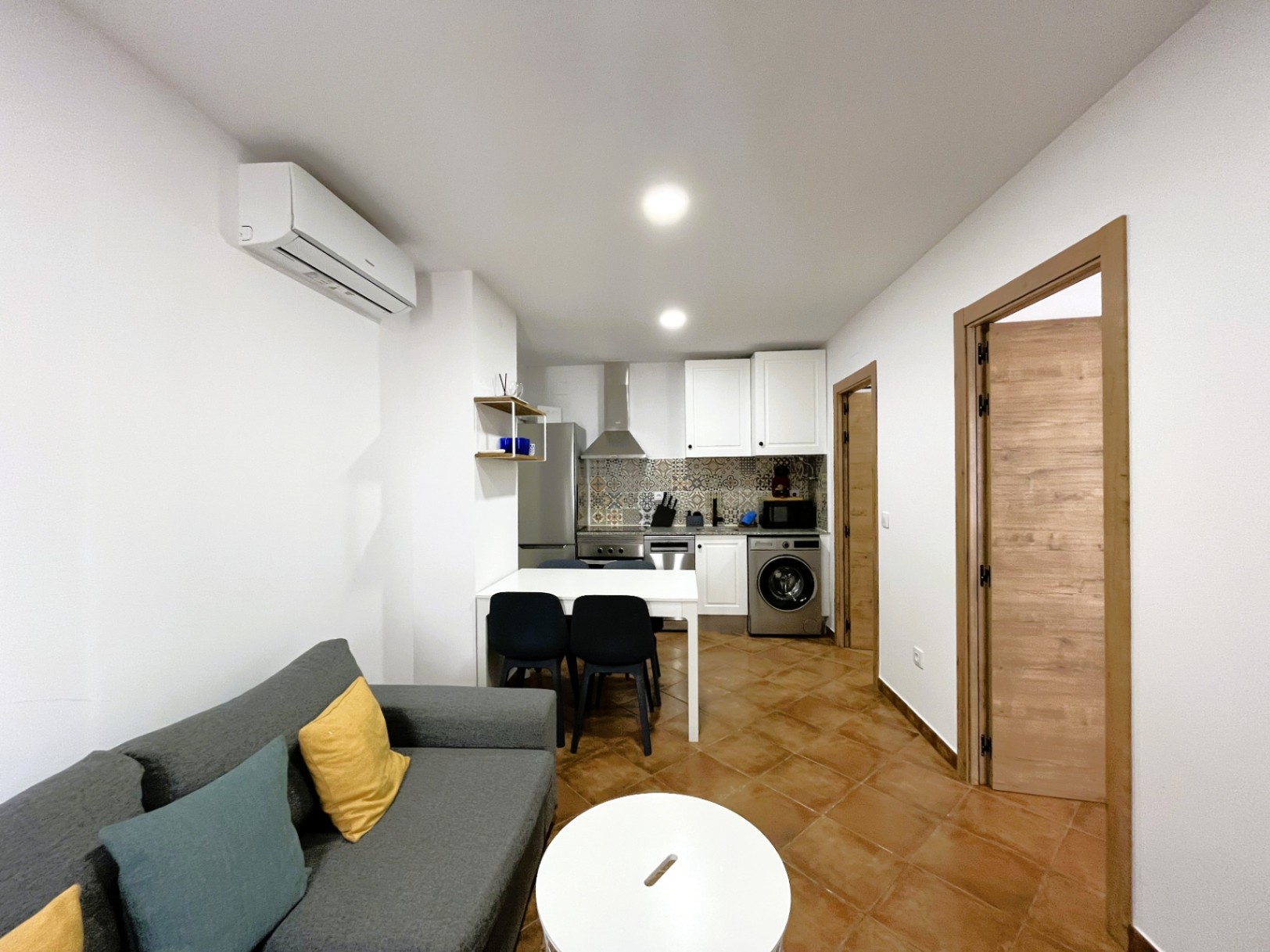 Open-plan living area featuring a kitchen with patterned tile backsplash, split air conditioning, and rustic terracotta-style flooring.