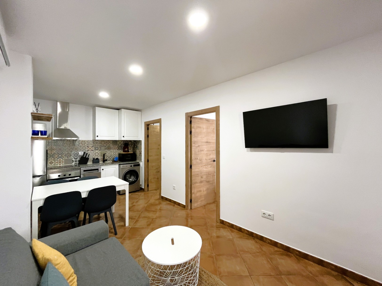 Open-plan living area featuring a modern kitchen with patterned tiles, recessed ceiling lights, and terracotta-style flooring throughout.